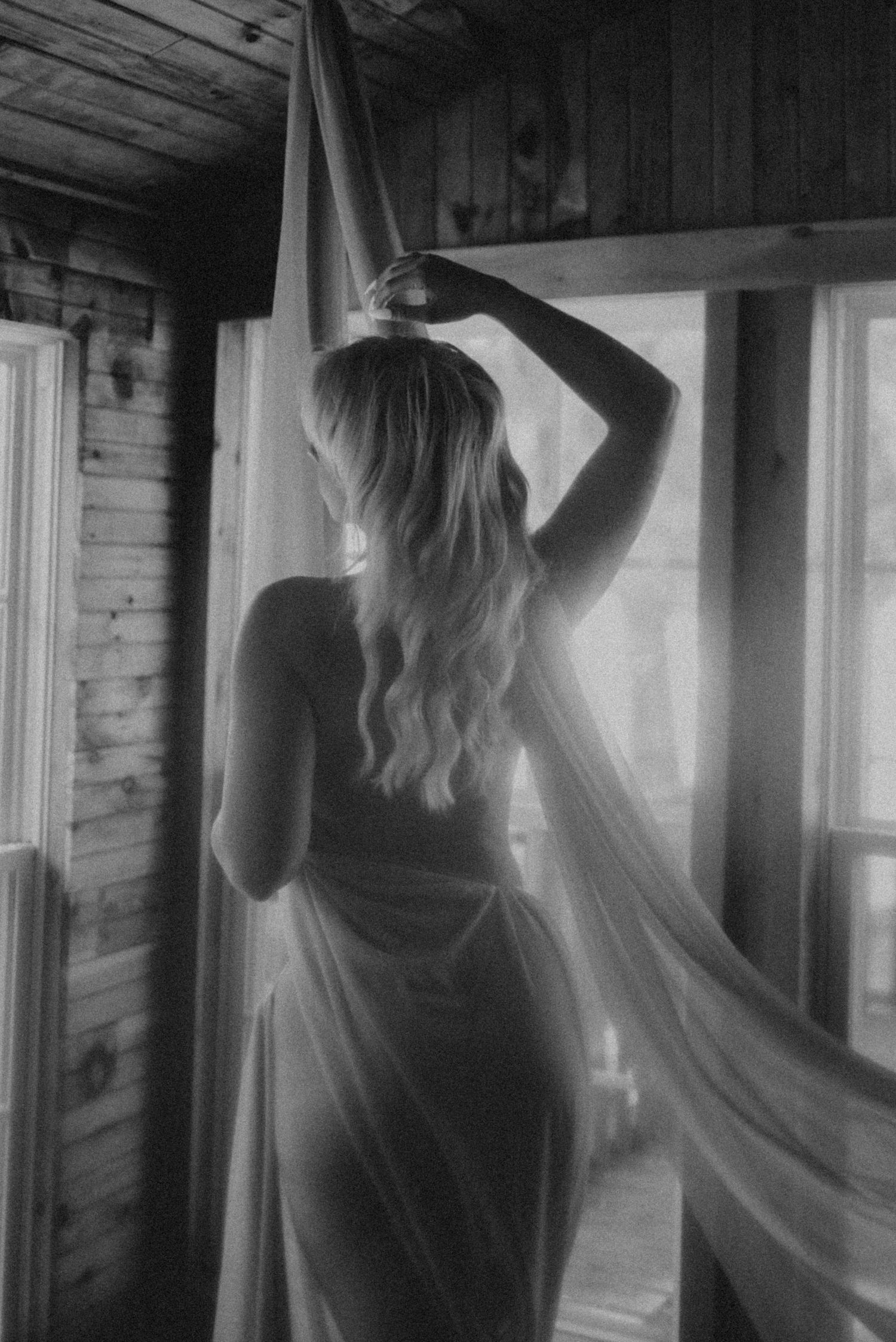 Black and white artistic portrait with dramatic window lighting in wooden room.