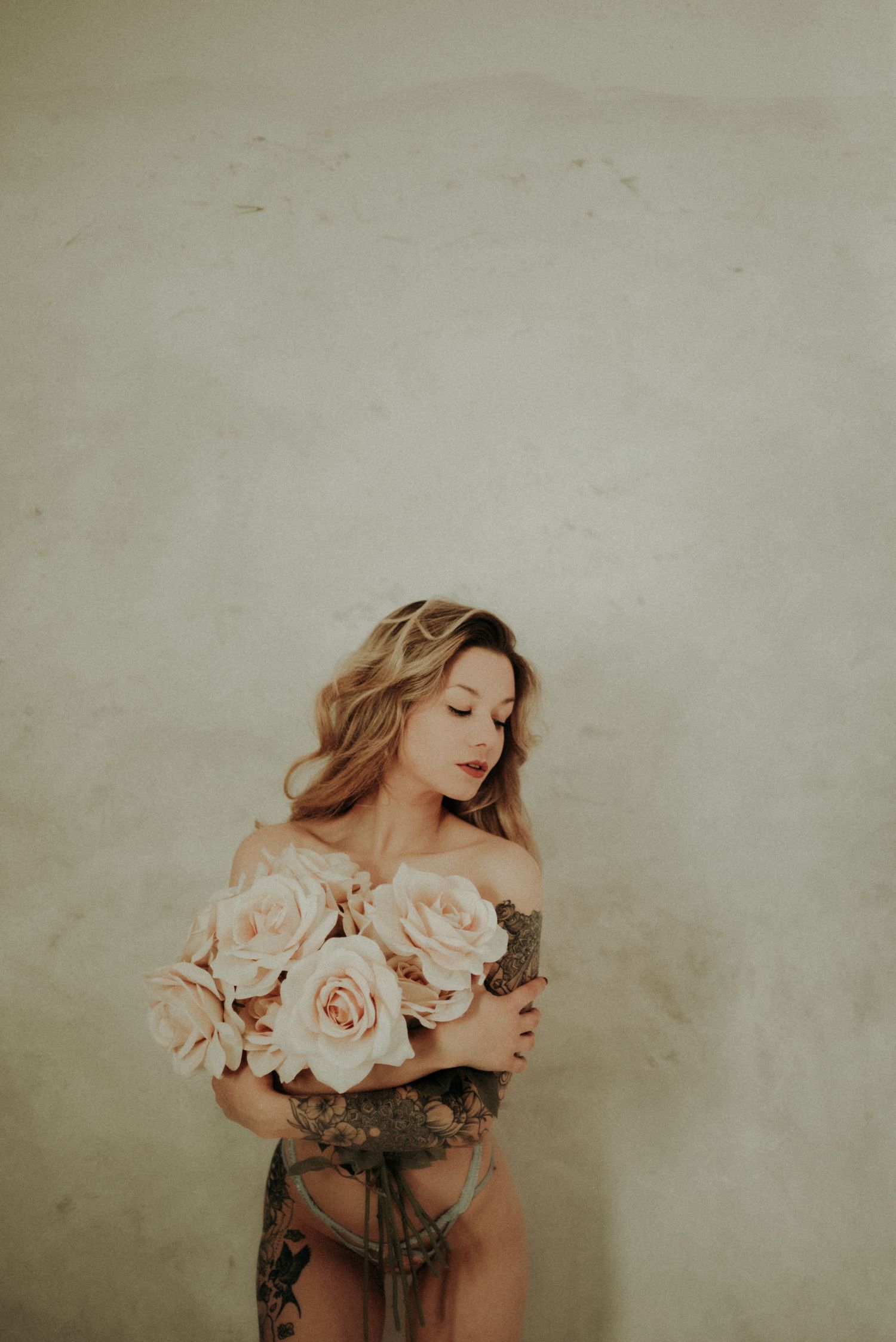 Artistic boudoir photo featuring soft pink roses against a neutral background.