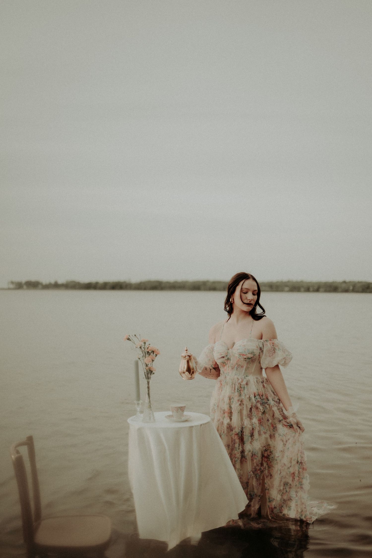 Romantic lakeside scene with vintage furniture and table settings at water's edge.