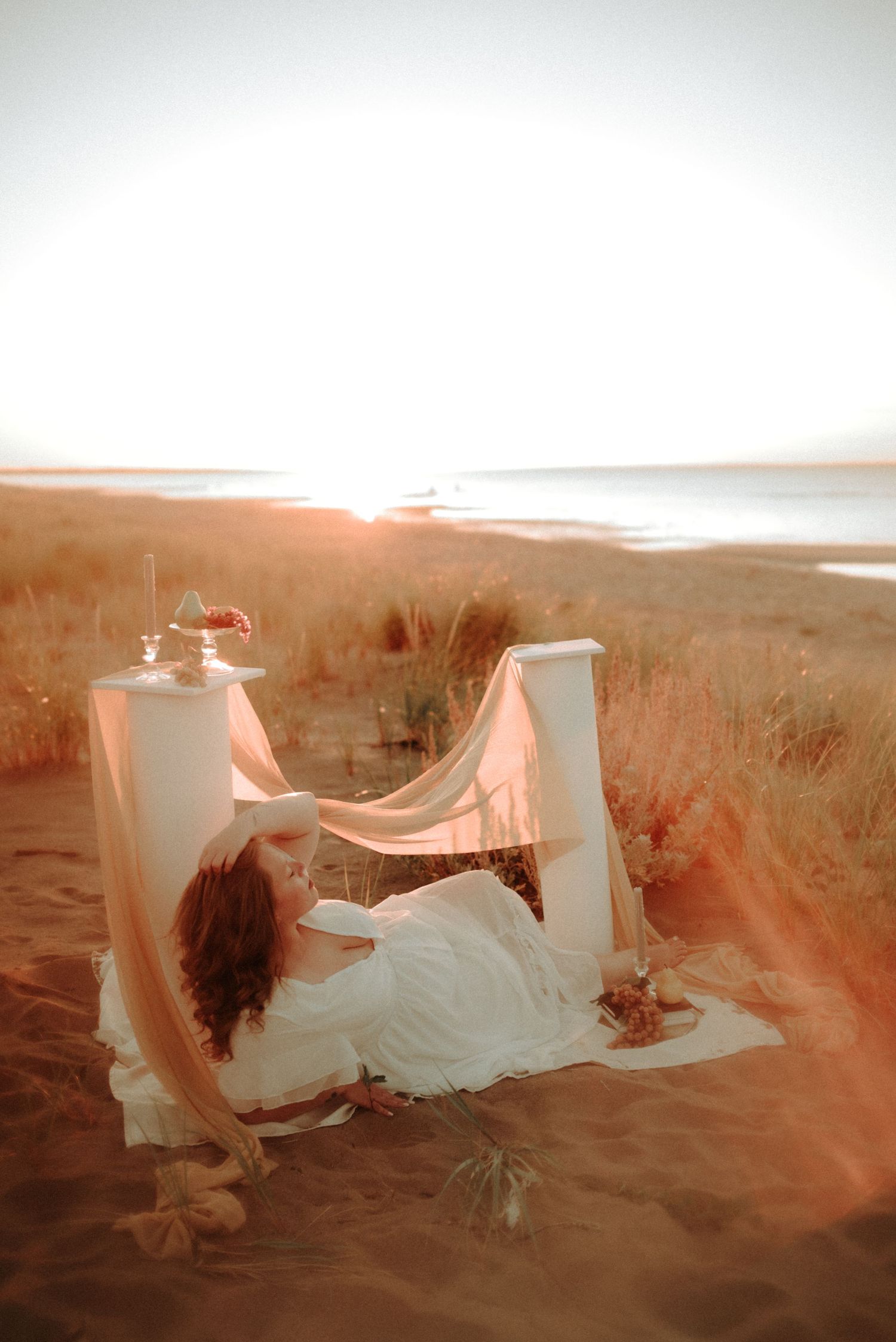 Ethereal scene of flowing white fabric among tall white columns at golden hour in a desert landscape.