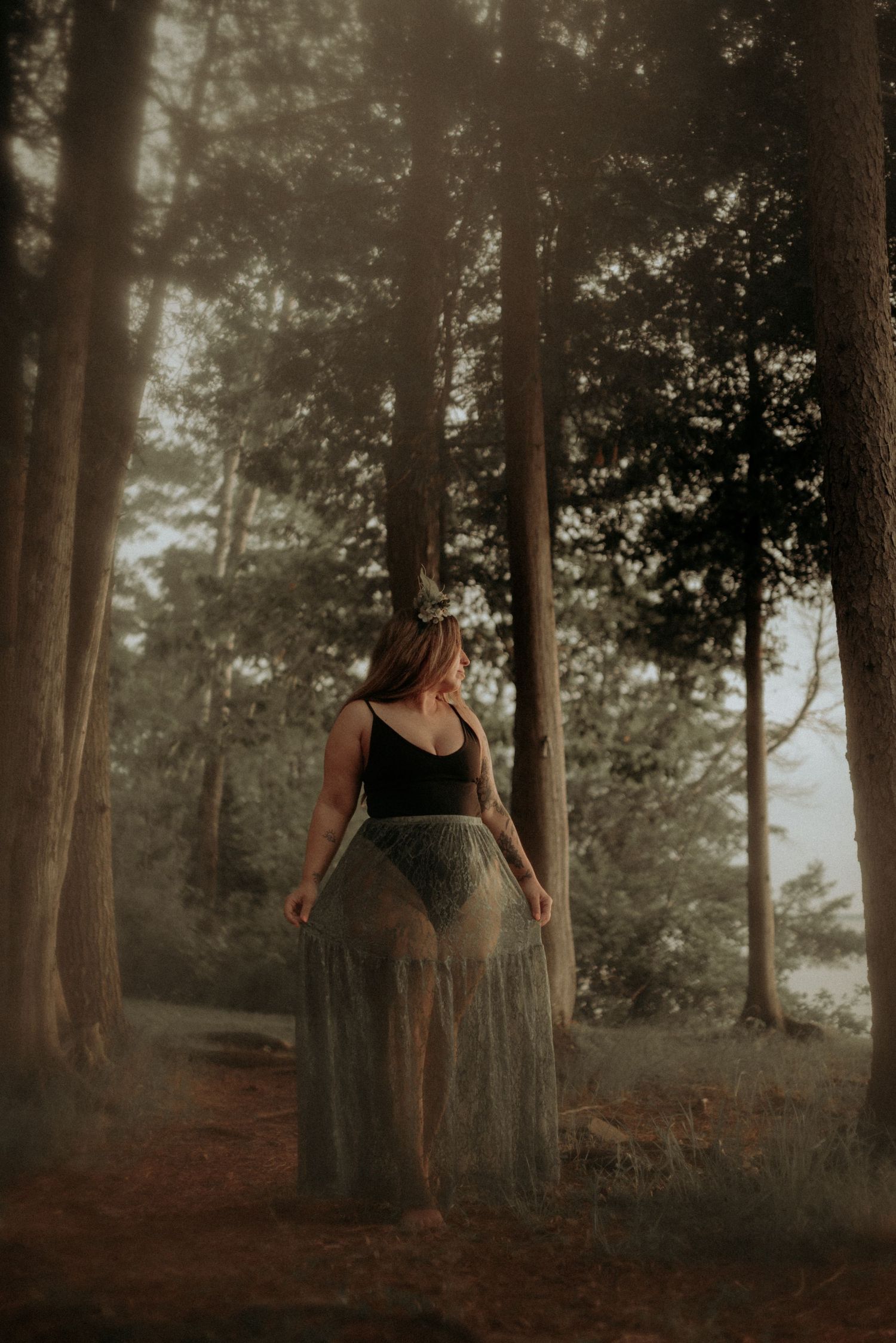 Enchanted forest photography with soft light filtering through trees and a flowing sheer dress.