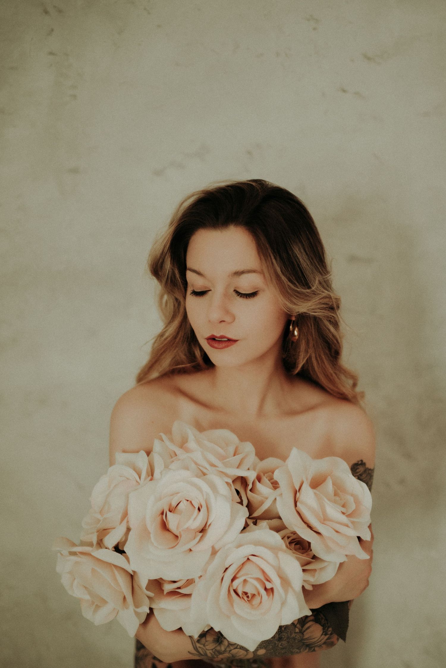 Romantic portrait with soft peach roses held against bare shoulders in a dreamy vintage aesthetic.