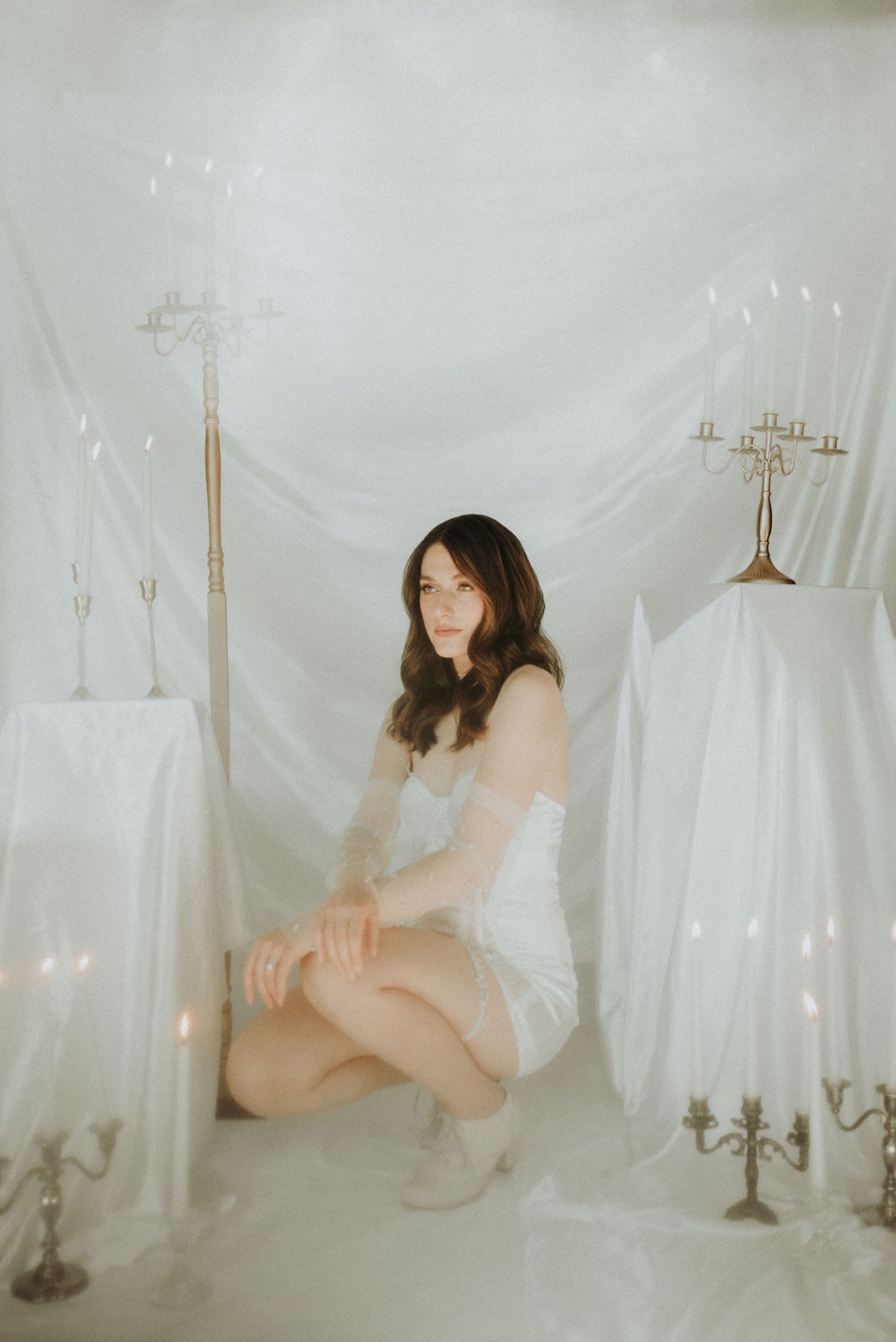 Ethereal boudoir photoshoot with white fabric backdrop and vintage candelabras creating a dreamy atmosphere.