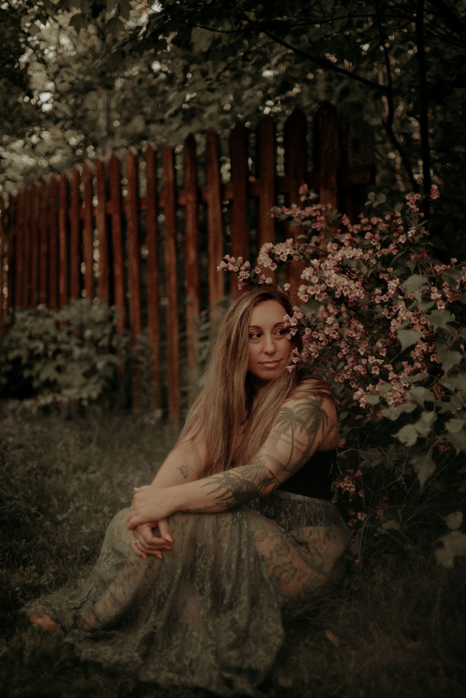 Dreamy portrait by wooden fence surrounded by spring blossoms in muted tones.
