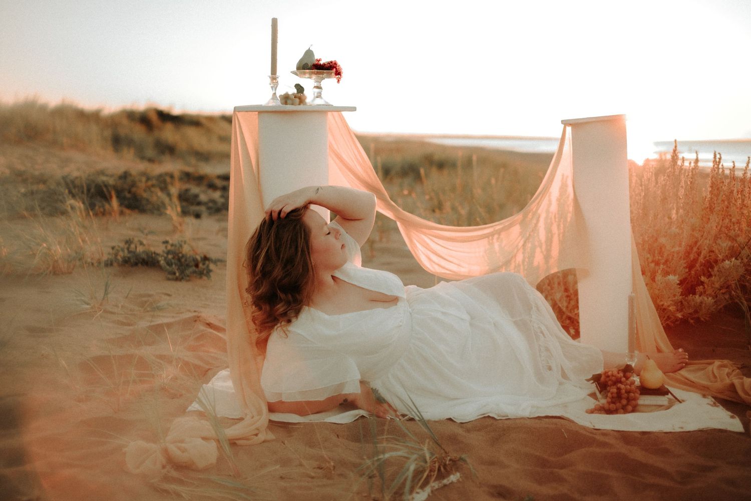 Elegant bridal photoshoot in golden desert landscape during sunset with flowing white dress and veil in soft light.