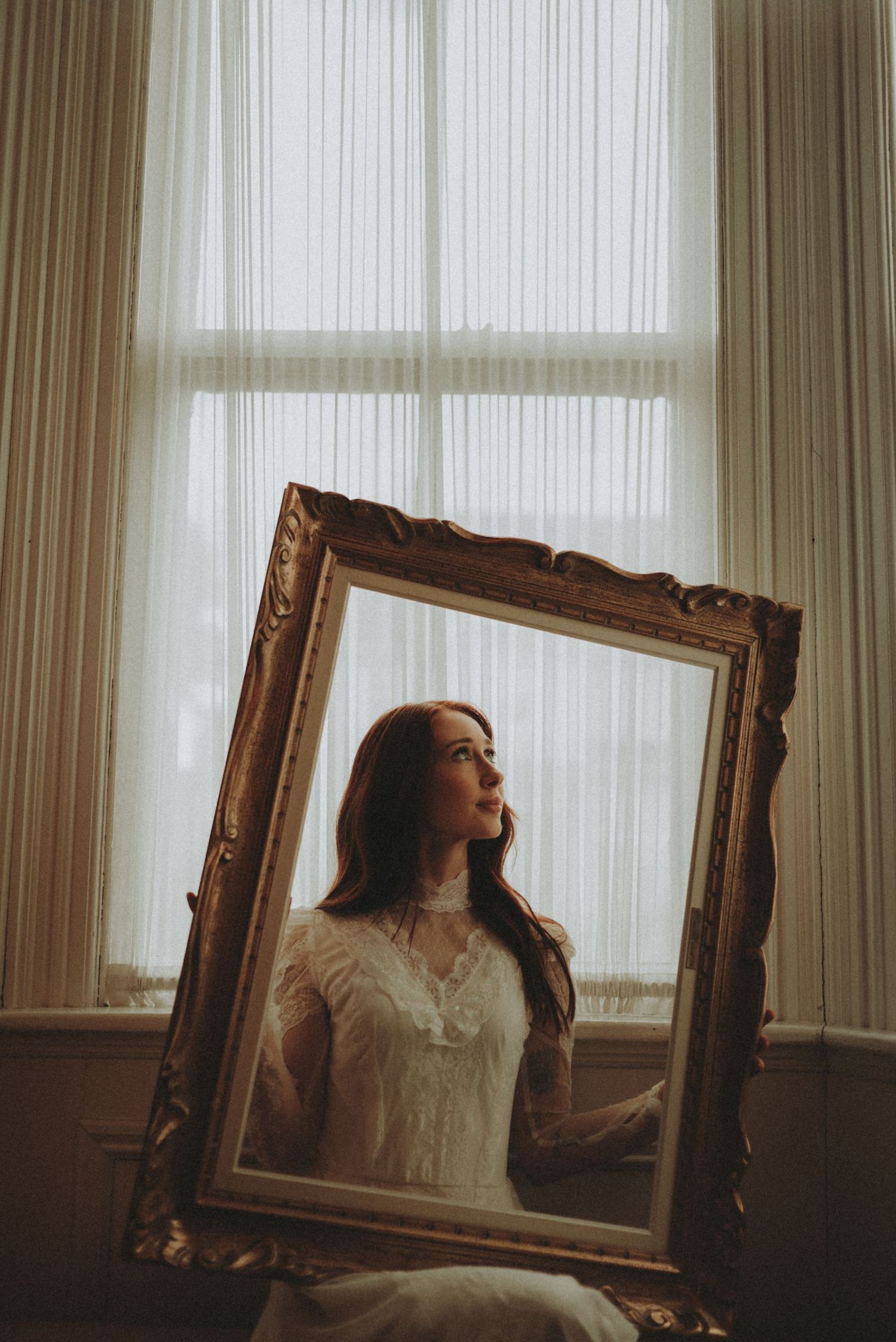 Artistic wedding portraits with empty gold frames creating reflective compositions by a bright window.