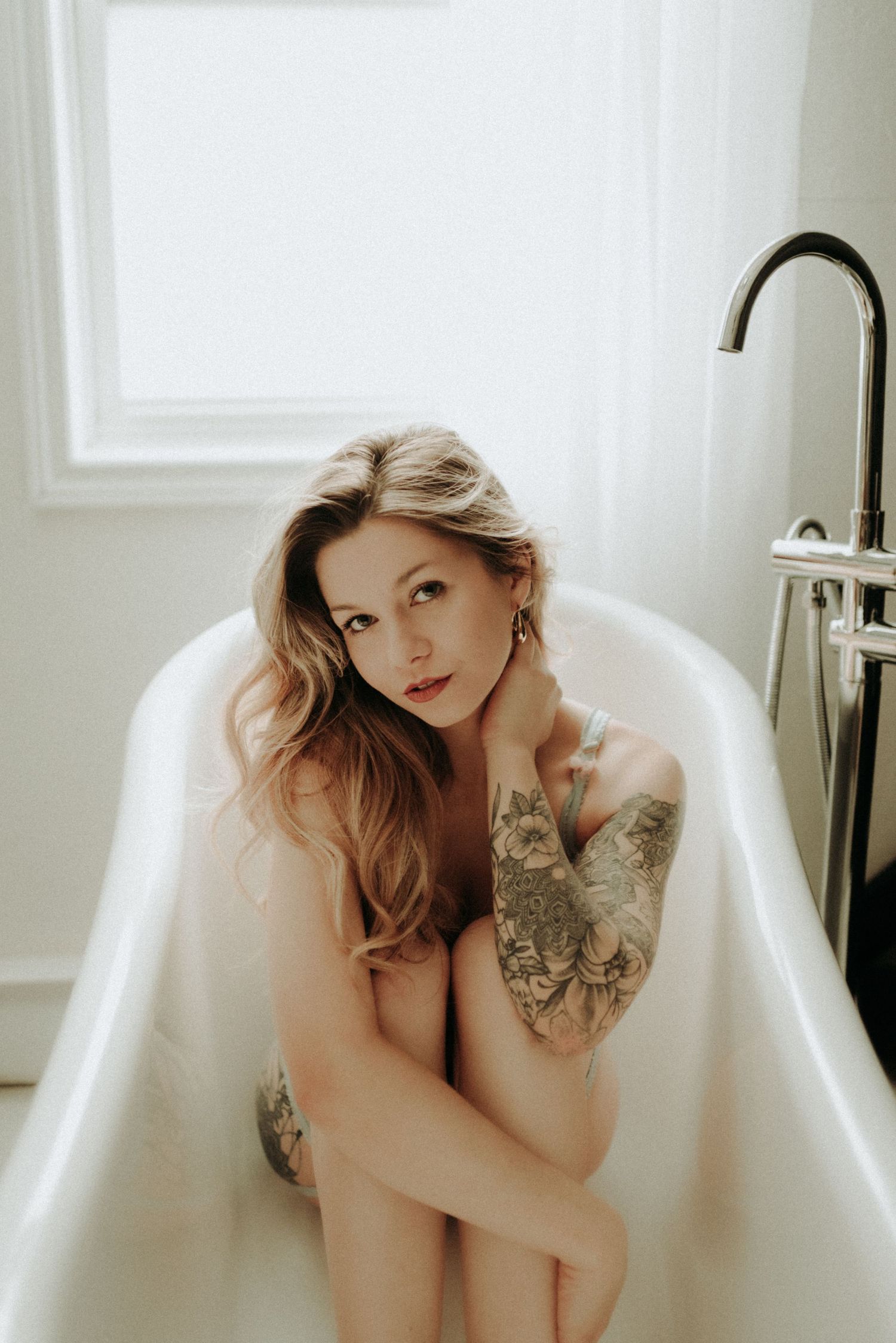 Artistic bathtub portrait with delicate lighting and tattoo details.