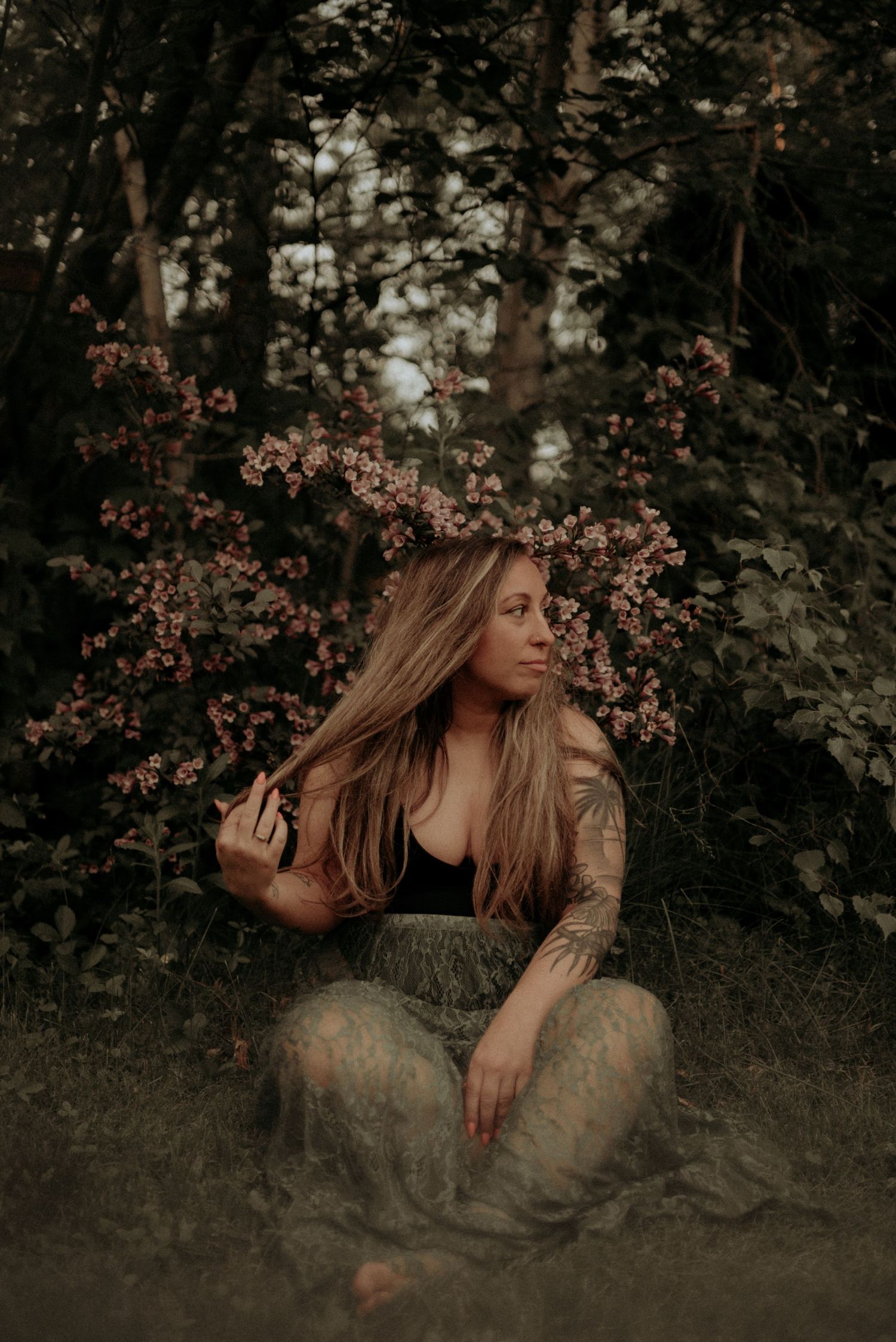 Moody forest portrait with flowering branches and long flowing dress in sepia tones.