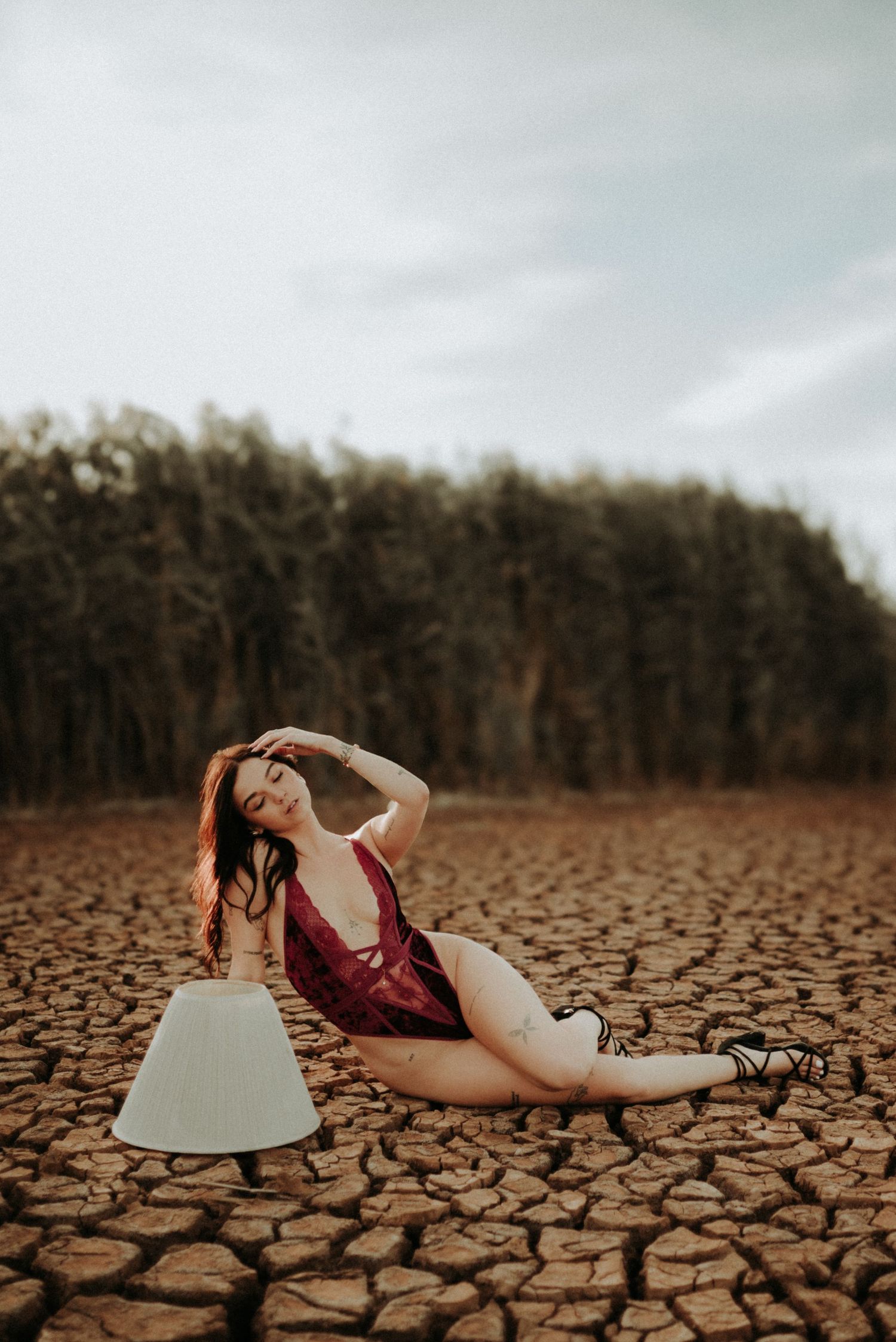 A figure in a red dress reclines dramatically on cracked, dry desert earth under a moody sky.