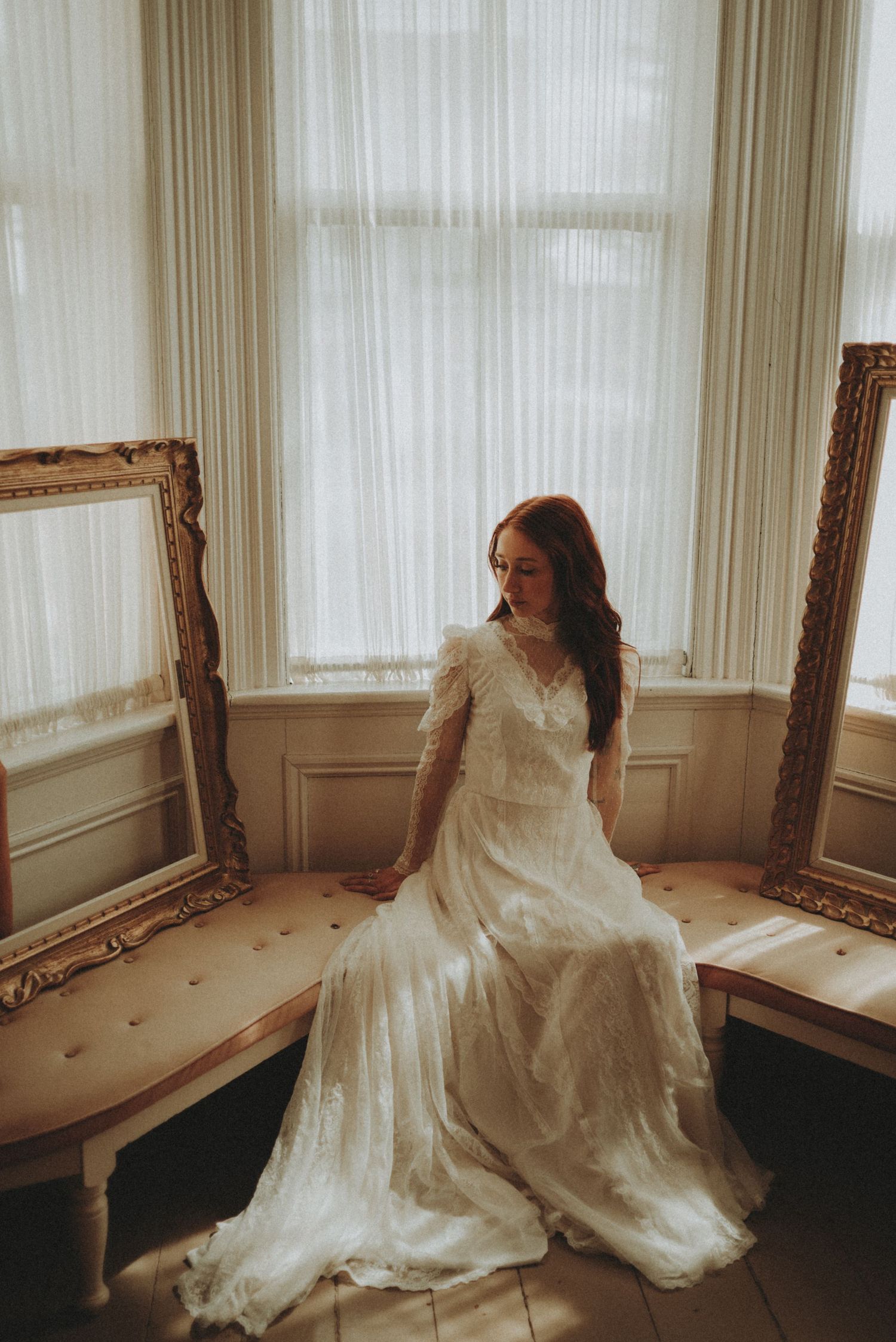 A romantic vintage-style bridal portrait in a sunlit room with ornate gold frames and sheer curtains.