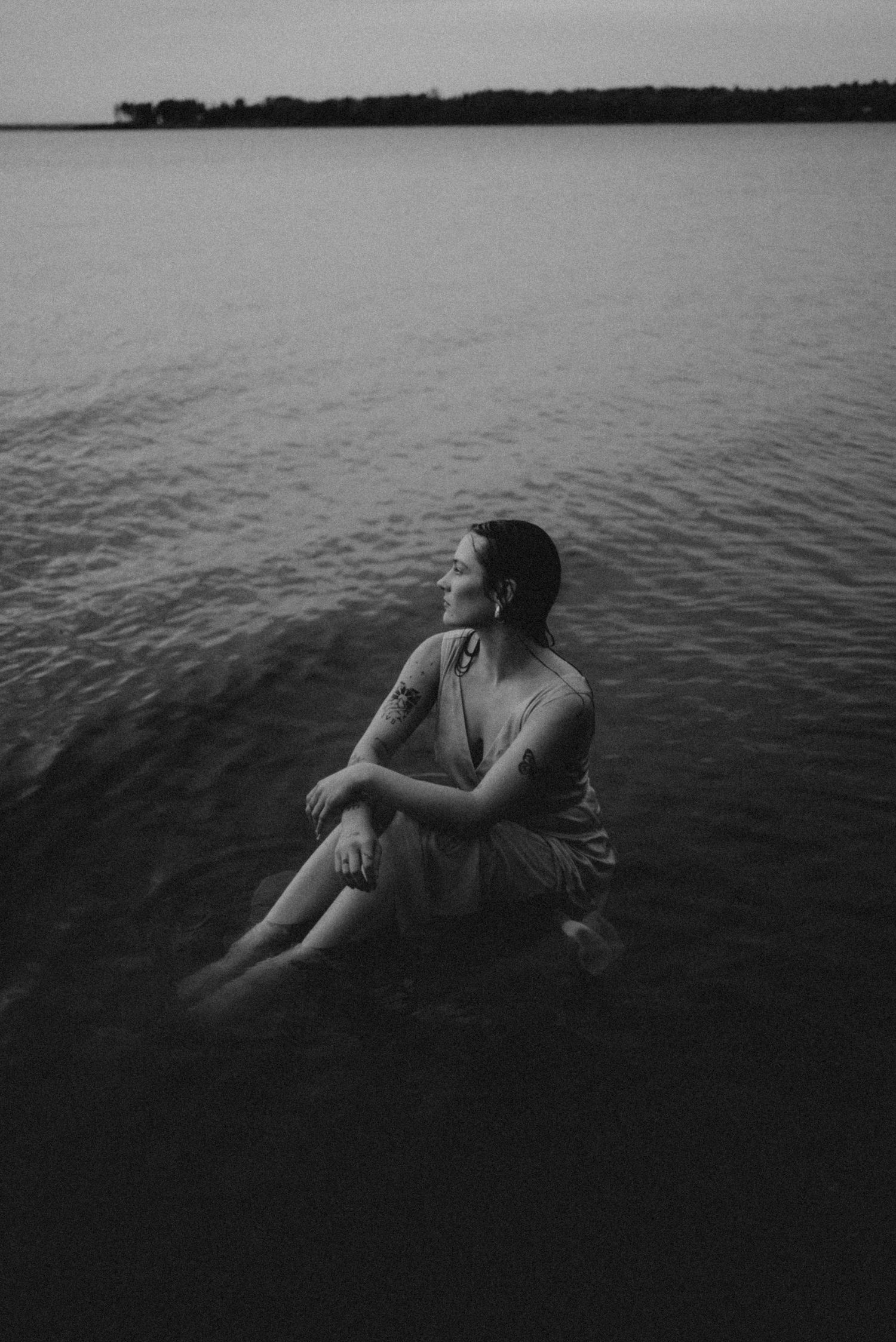 Black and white lake portrait showing a person sitting in calm waters at dusk.