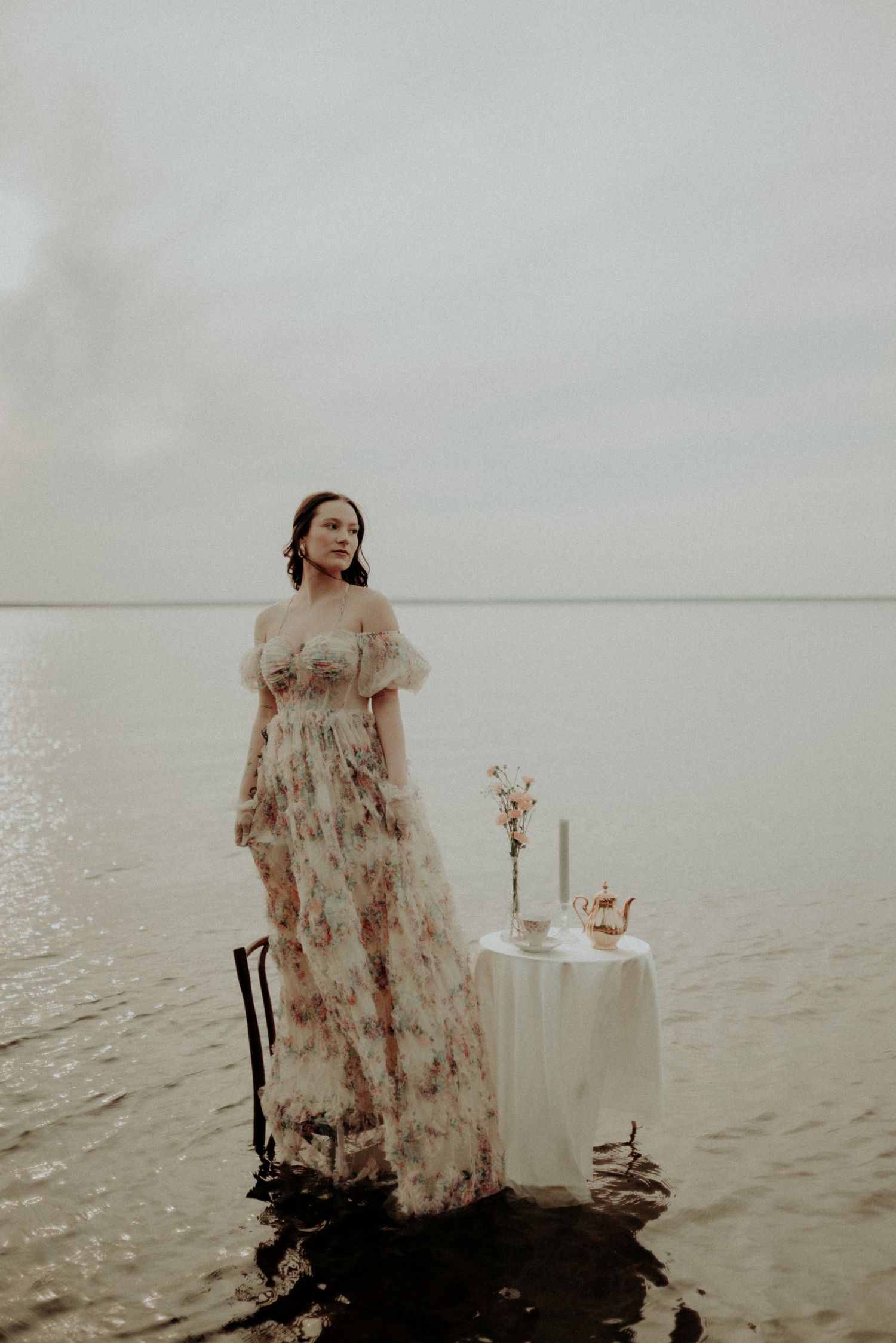 Moody fashion photography with vintage-inspired dress and table setting in shallow waters.