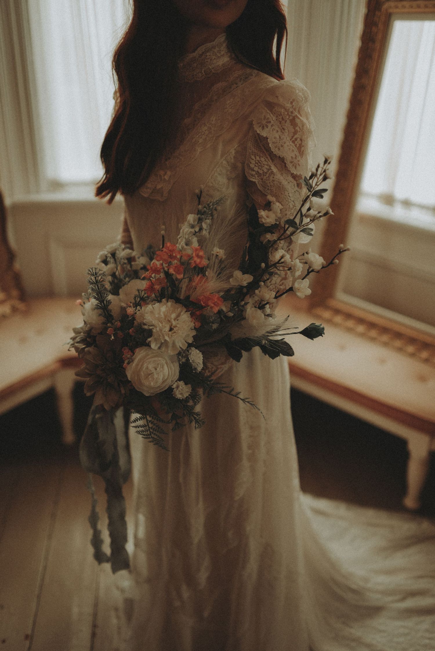 A detailed shot captures an elegant wedding bouquet of roses and foliage against a delicate lace wedding dress.
