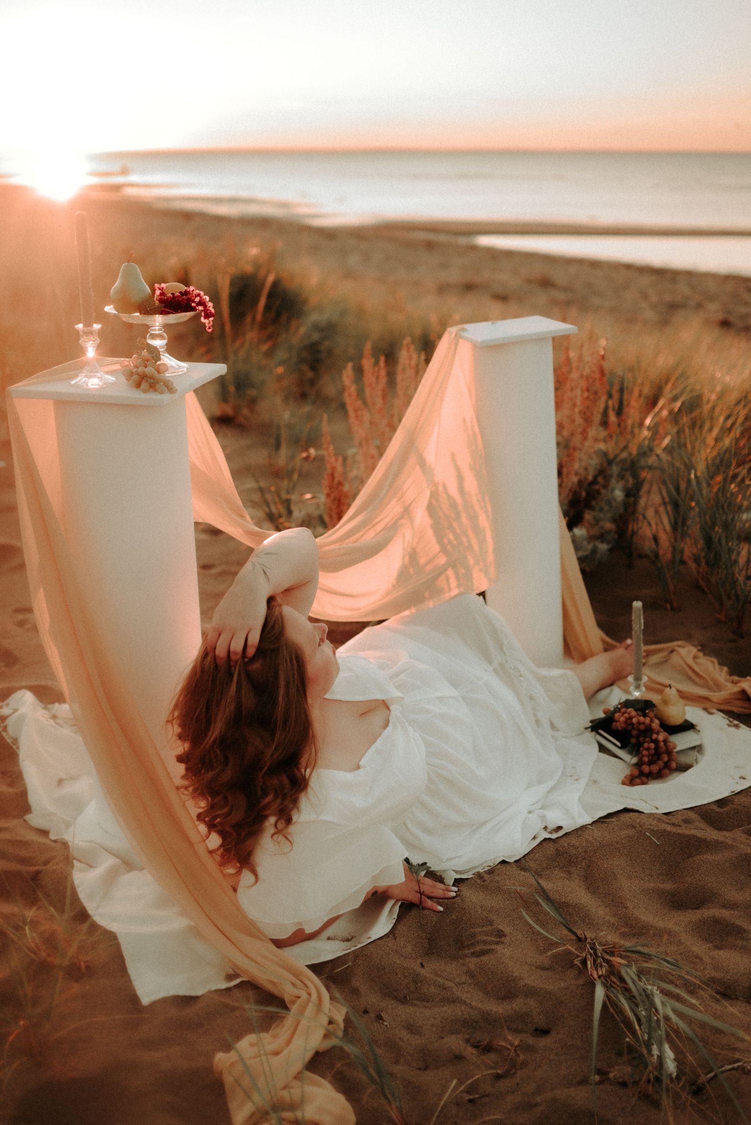 Dreamy coastal photoshoot featuring white pillars and flowing fabric during sunset.