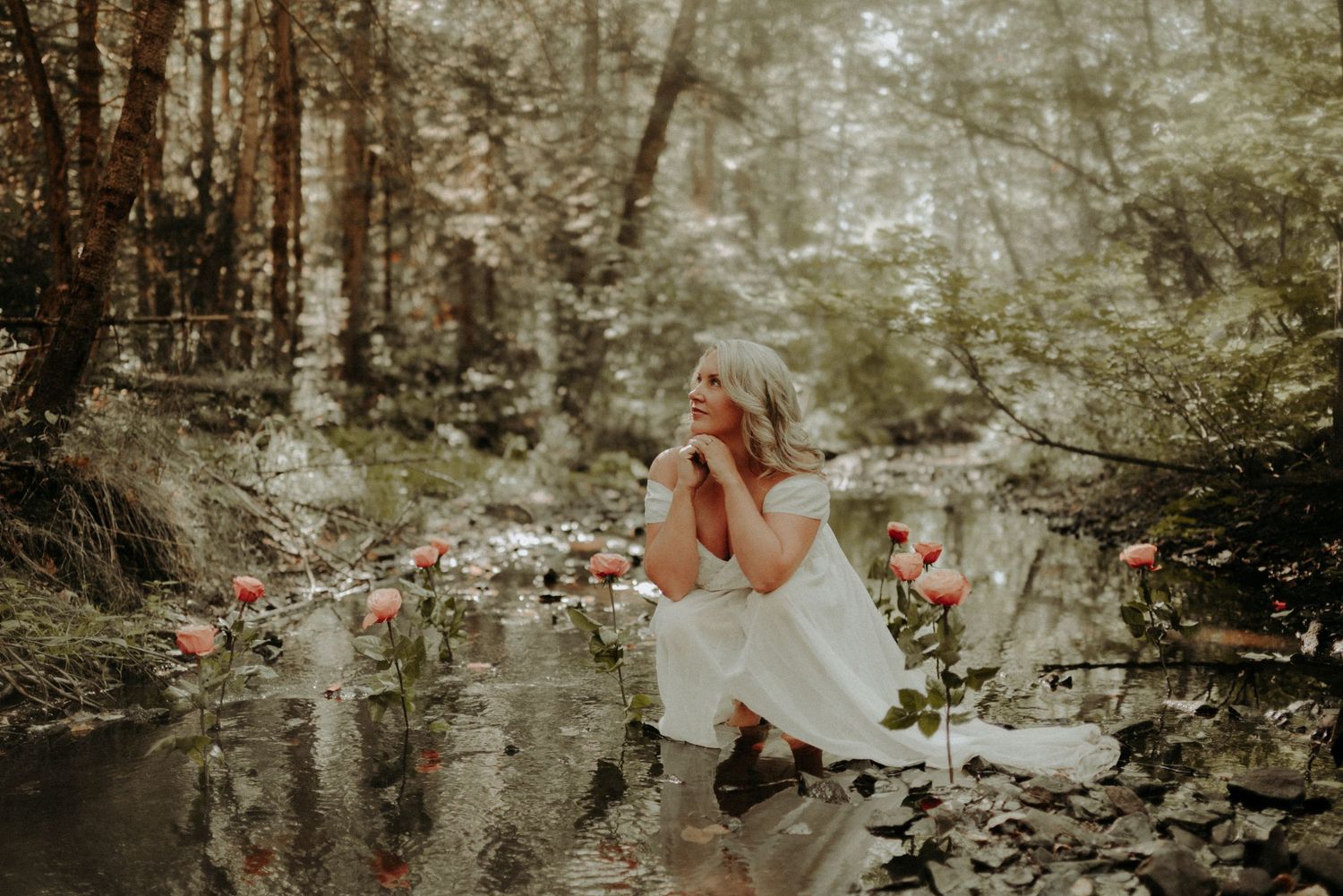 Ethereal woodland scene with a person in white dress sitting by a reflective stream surrounded by pink flowers and forest foliage.