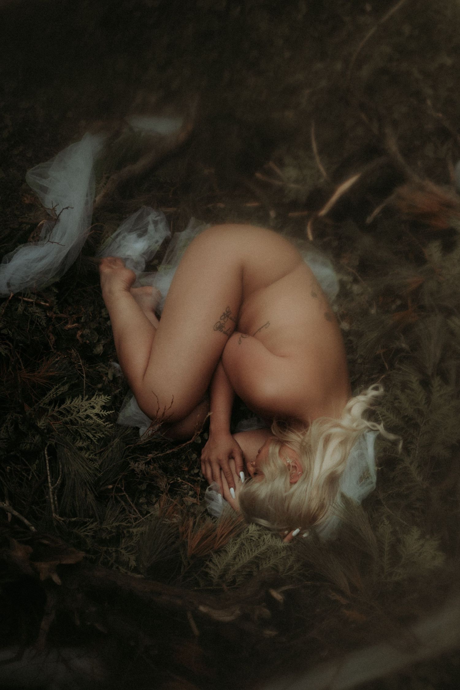 Artistic boudoir photograph with soft moody lighting in nature setting.
