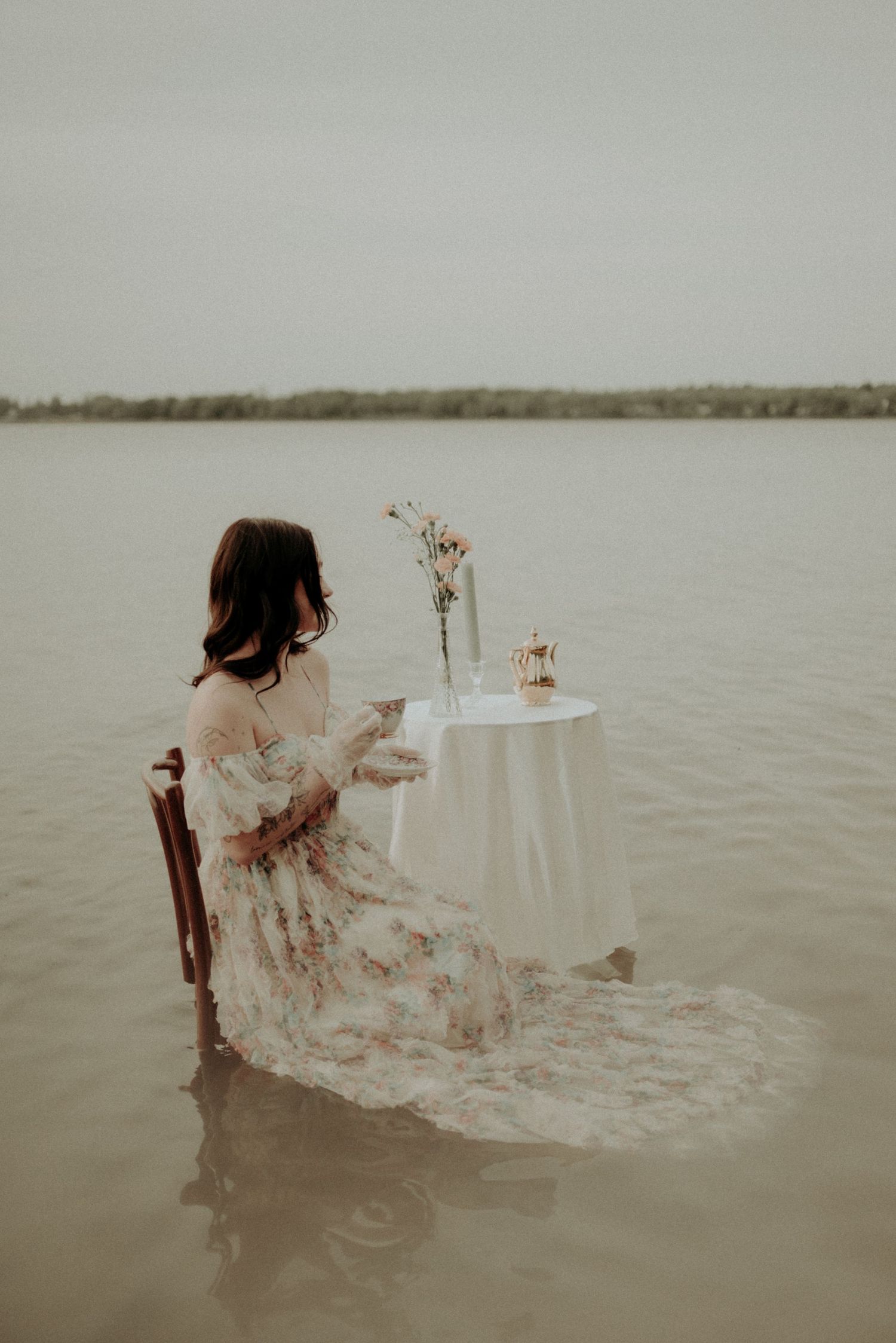 A romantic scene with flowing dress and white table setting in calm waters during golden hour.