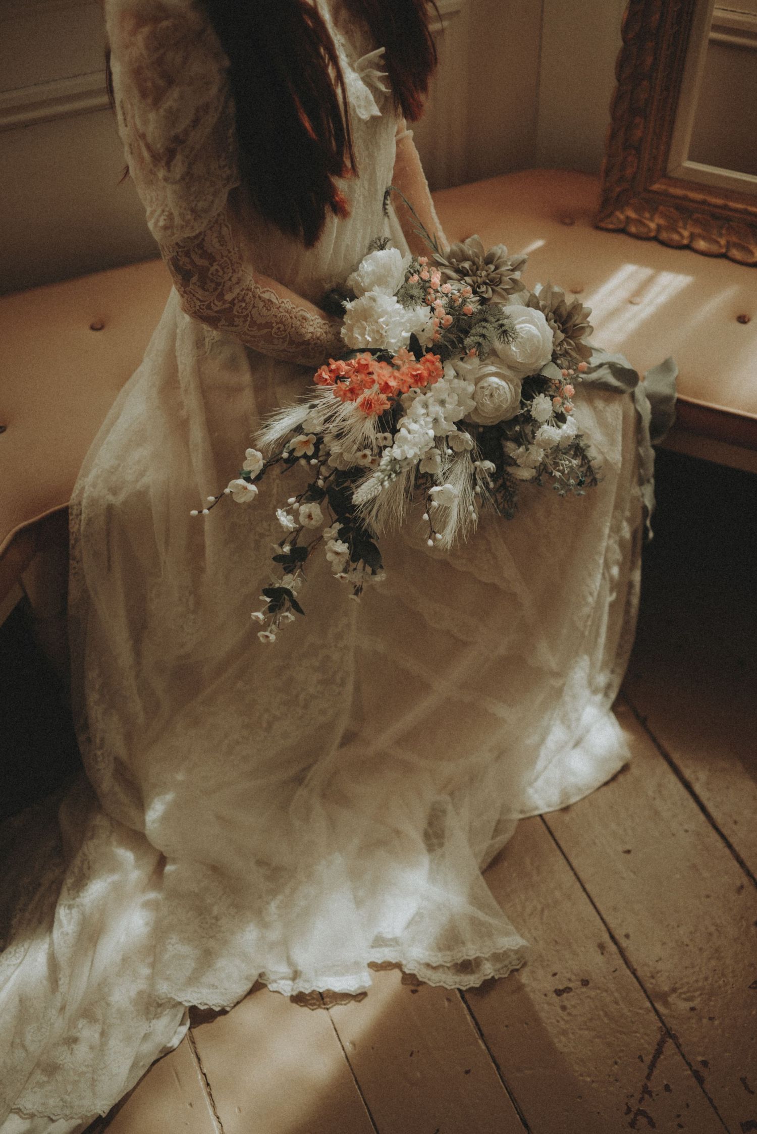 Romantic wedding dress detail with delicate floral arrangements on wooden floor in natural light.