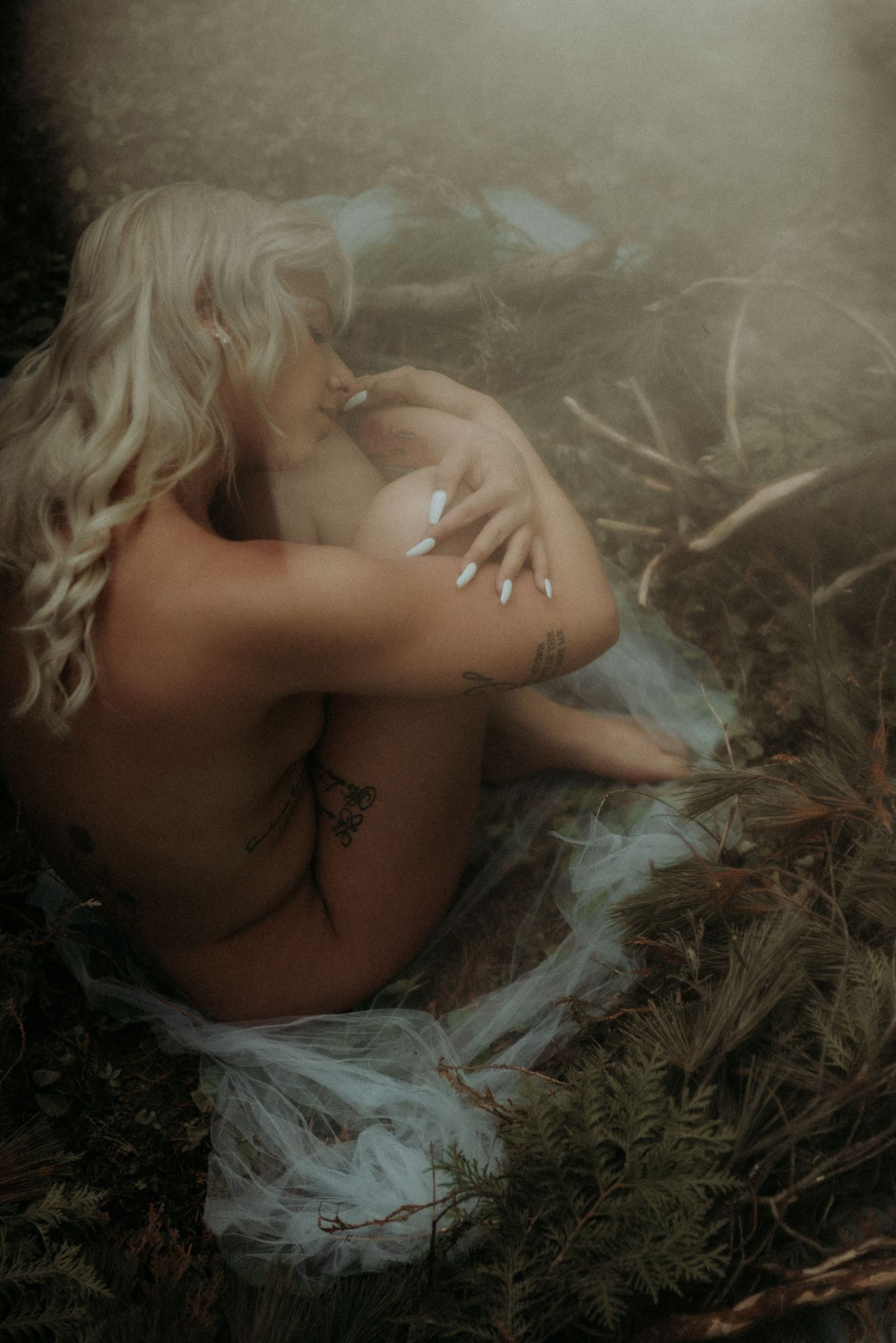 Intimate artistic portrait with delicate lighting and natural elements on ground.