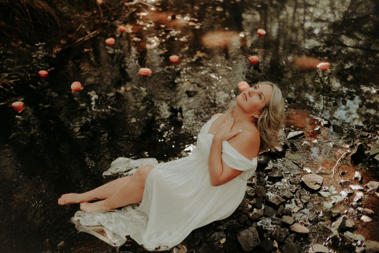 Ethereal figure in flowing white dress reclines on forest floor surrounded by autumn leaves and glowing lights.