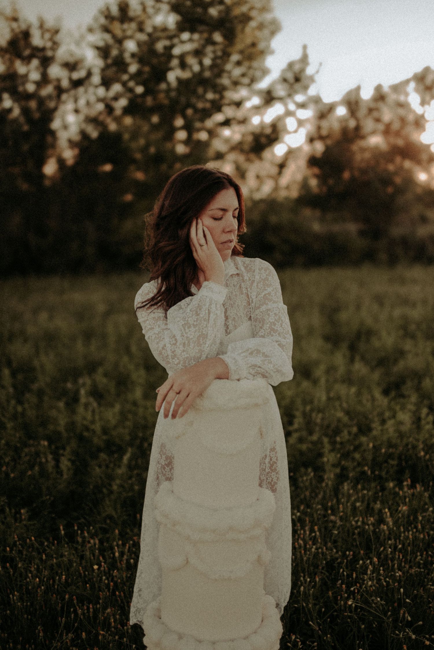 A person in a vintage white lace dress poses gracefully in a wildflower field at golden hour.