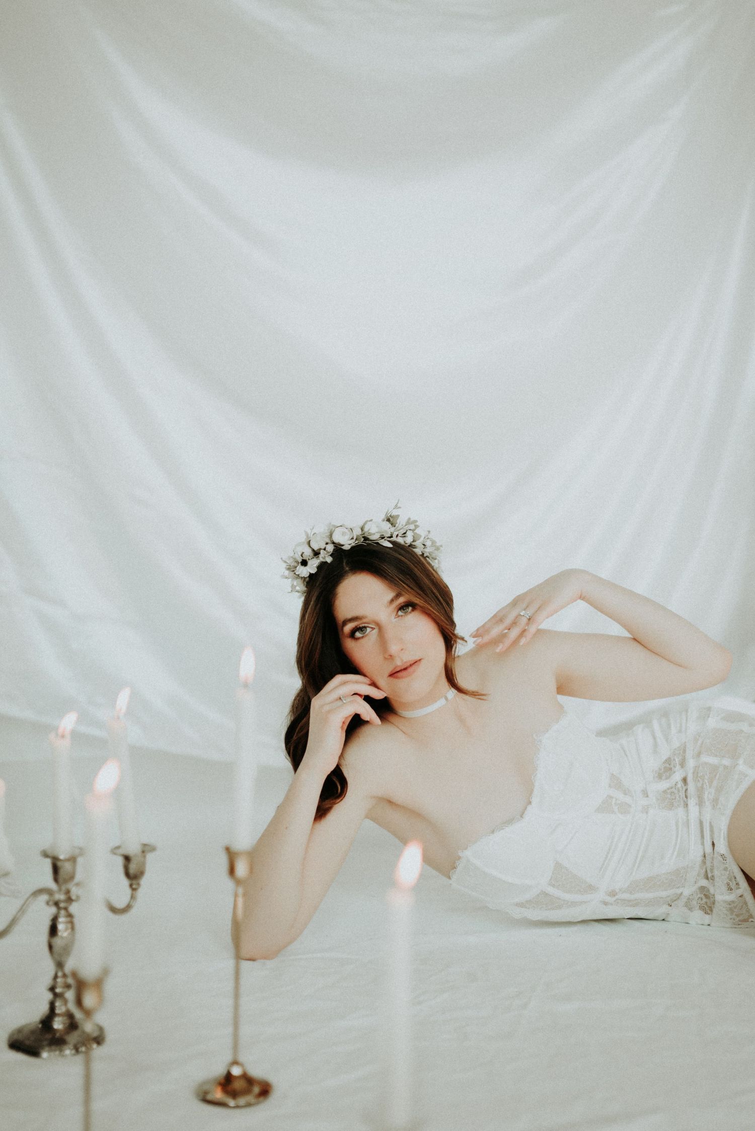 A dreamy boudoir photoshoot with soft white draping fabric, antique candelabras, and ethereal lighting creating a romantic mood.