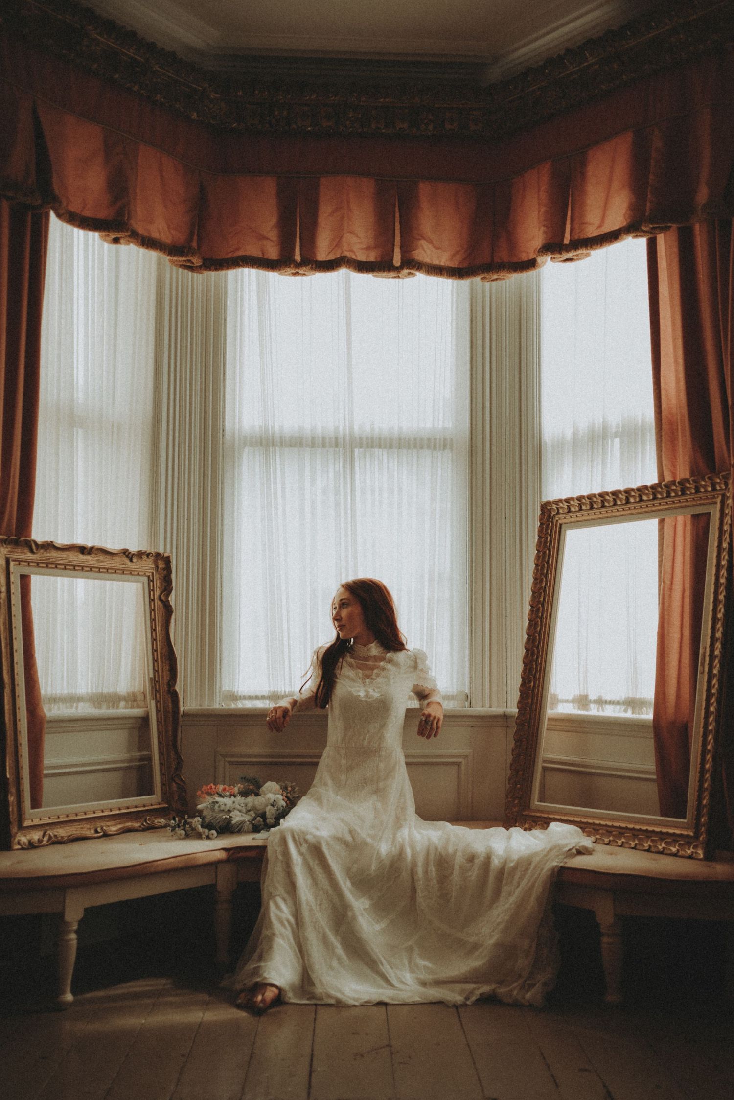 Artistic wedding photography in bay window setting with vintage decor and flowing white gown.