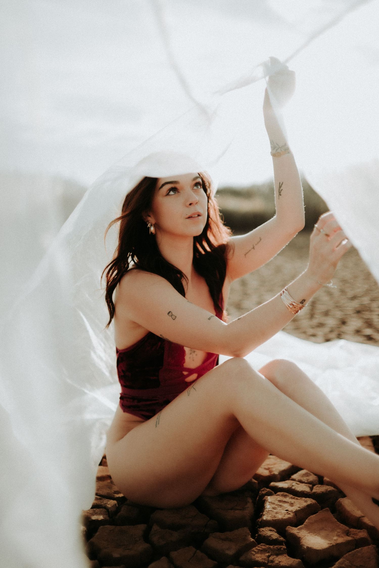 Woman in red swimwear poses gracefully on sandy beach during golden hour photoshoot.