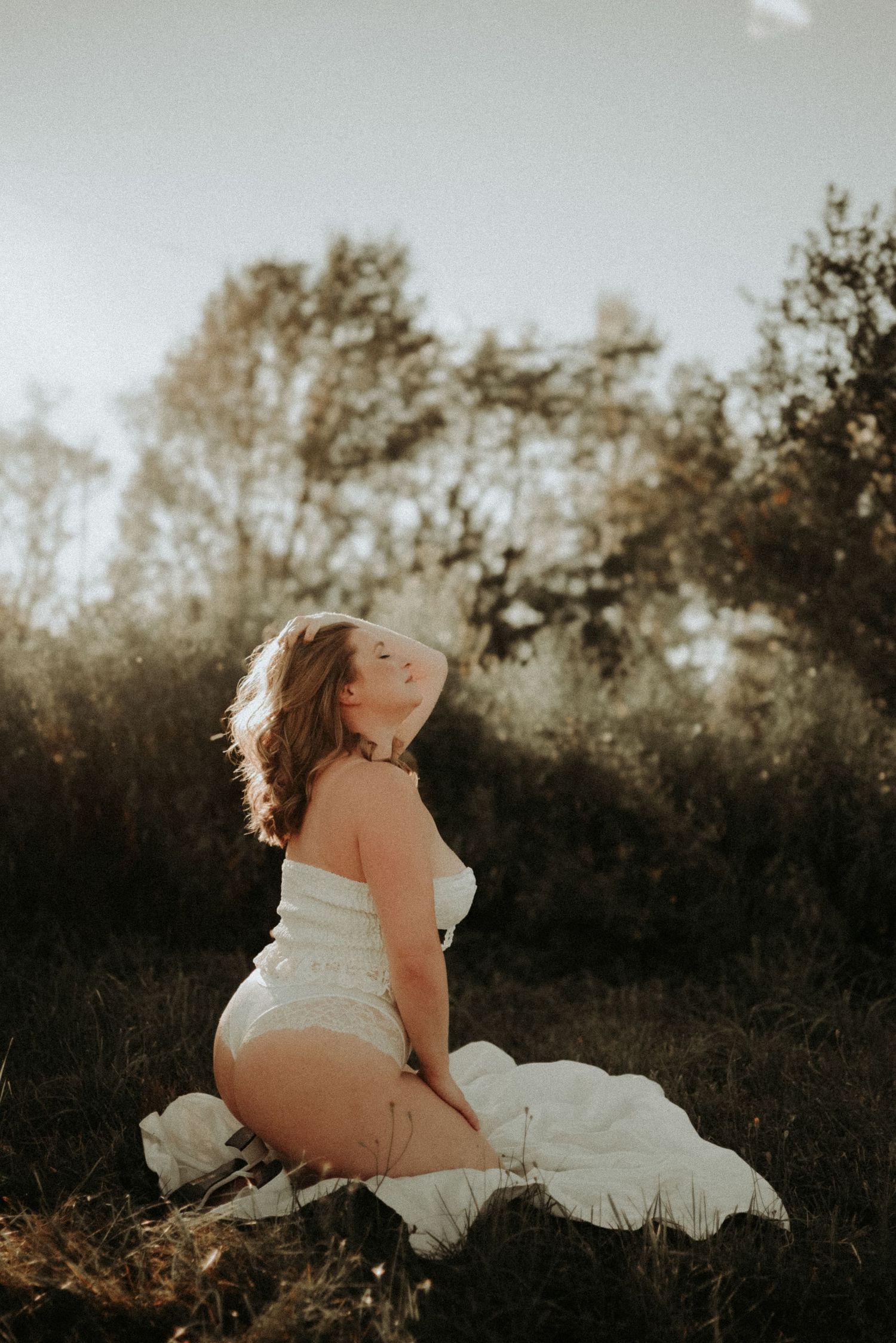 Artistic boudoir photography silhouette of person in white dress laying in field at sunset.