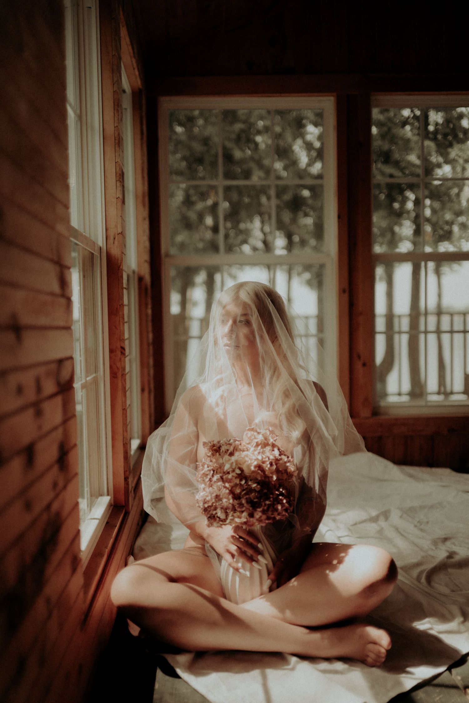 Romantic sunlit scene by a window with sheer fabric and dried flowers.