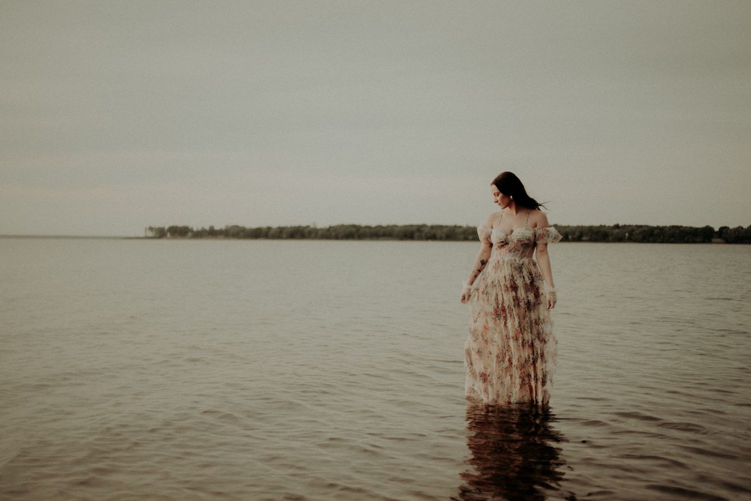 Silhouette of a person wearing a vintage dress while standing in calm lake waters.
