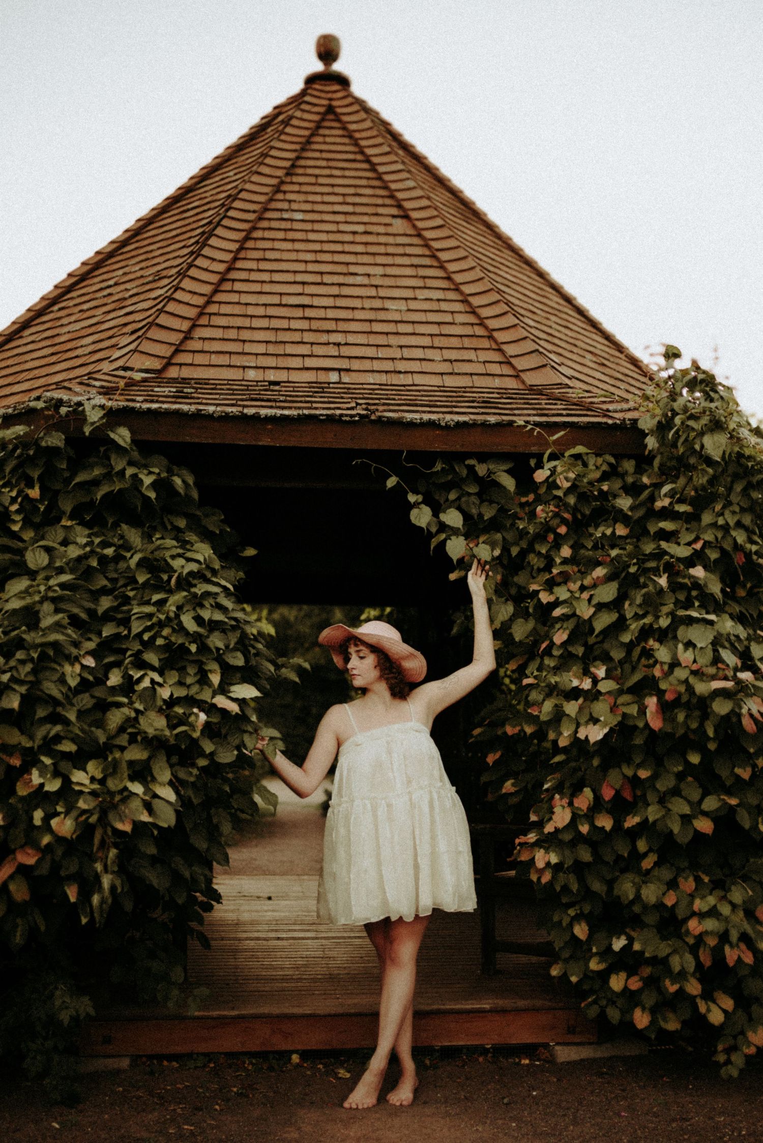 Artistic portrait under a wooden gazebo surrounded by climbing vines at dusk.