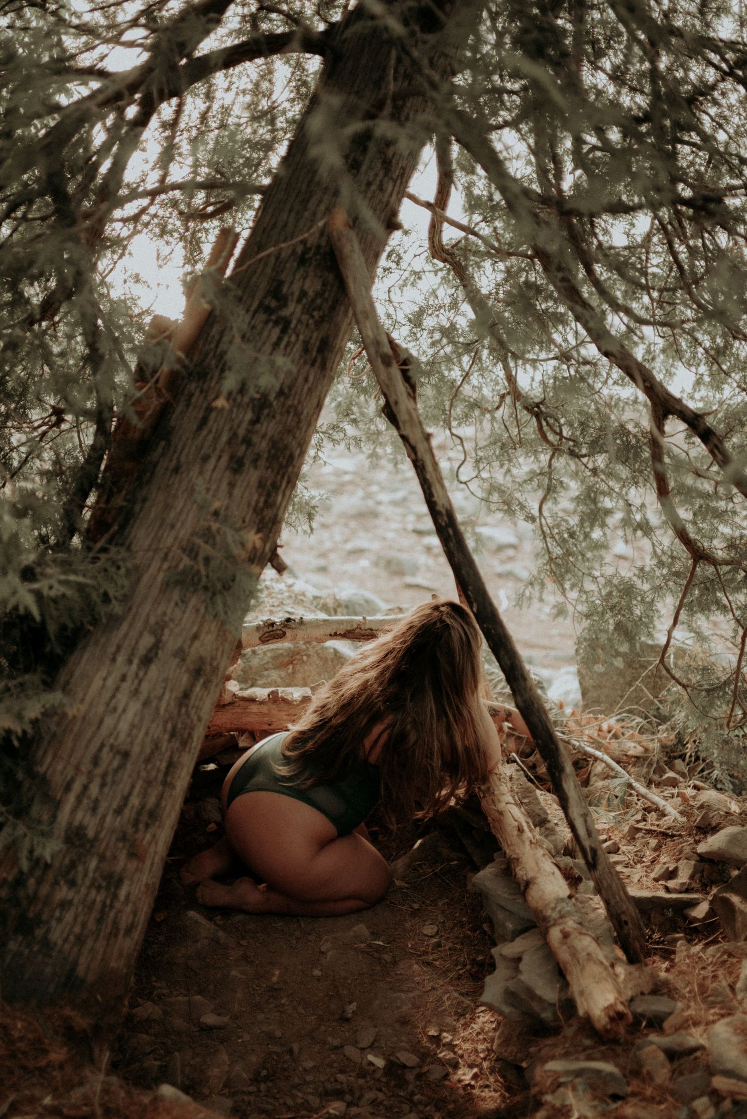 Artistic portrait under a natural wood shelter in a mystical forest setting.