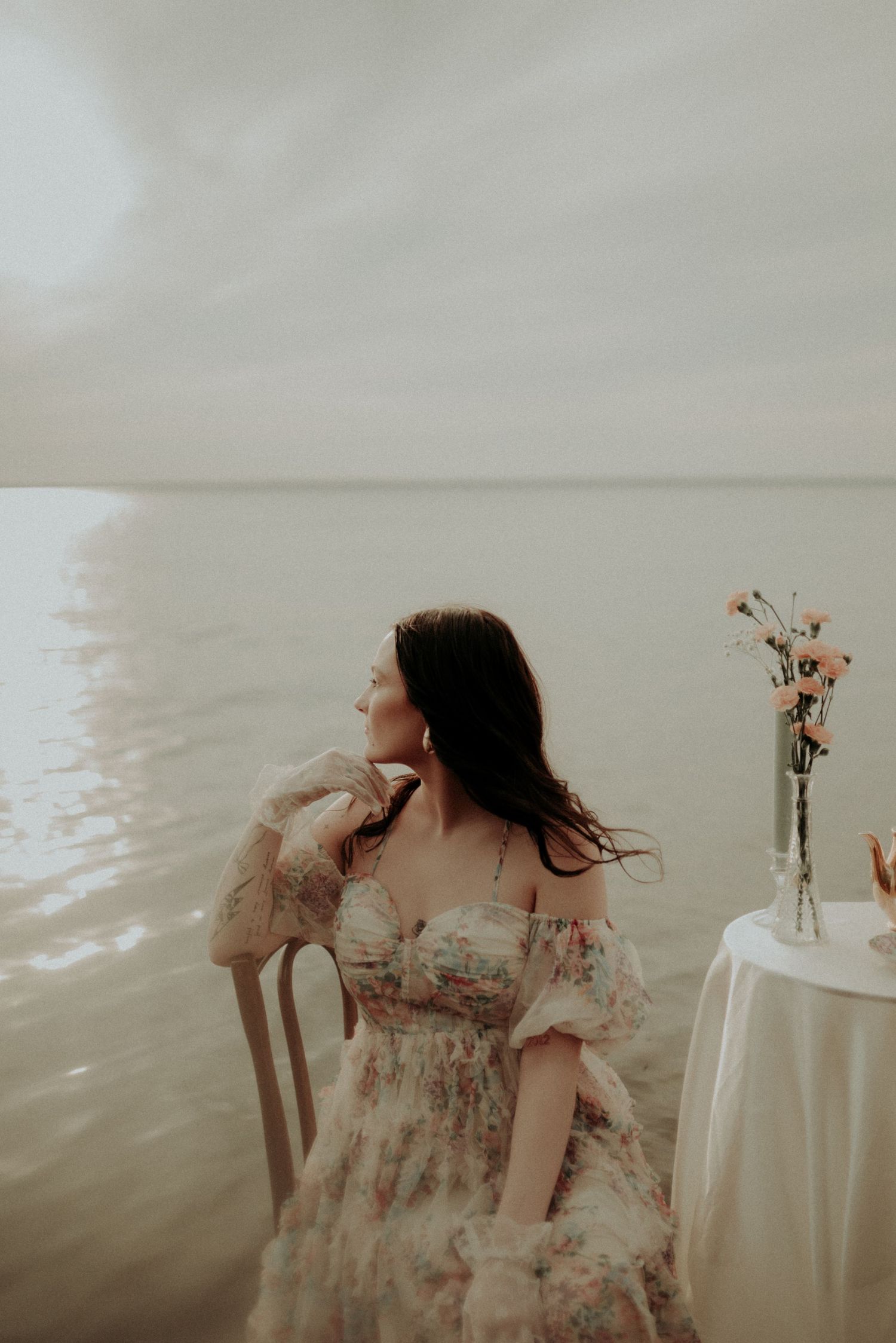 Romantic vintage-inspired portrait beside small table with dried flowers in soft lighting.