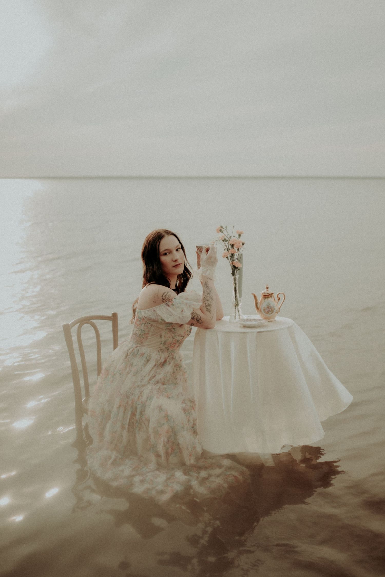 Artistic portrait session in water with vintage table settings and floating fabric creating movement.