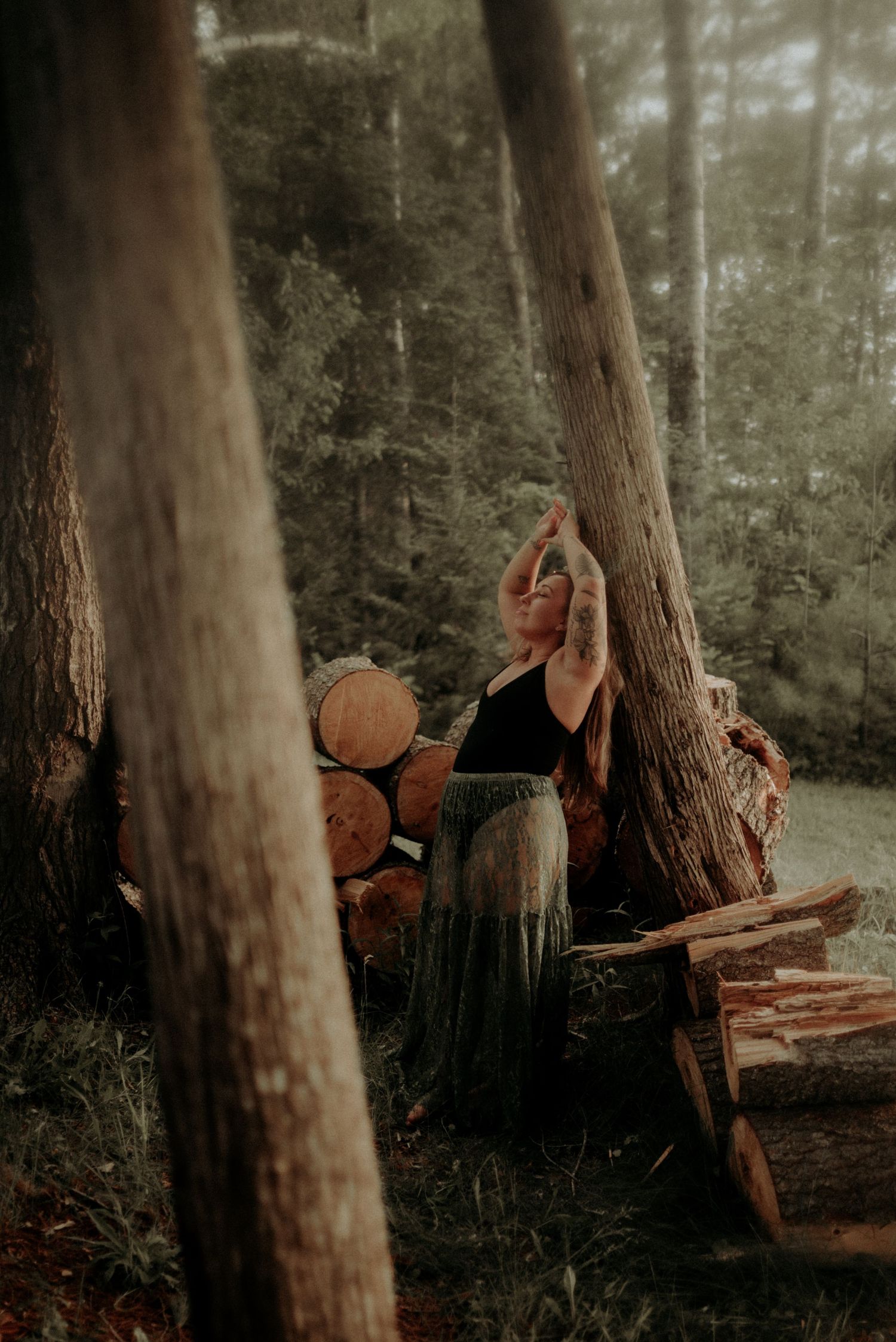 Enchanted forest scene with reaching pose against tall trees and stacked firewood.