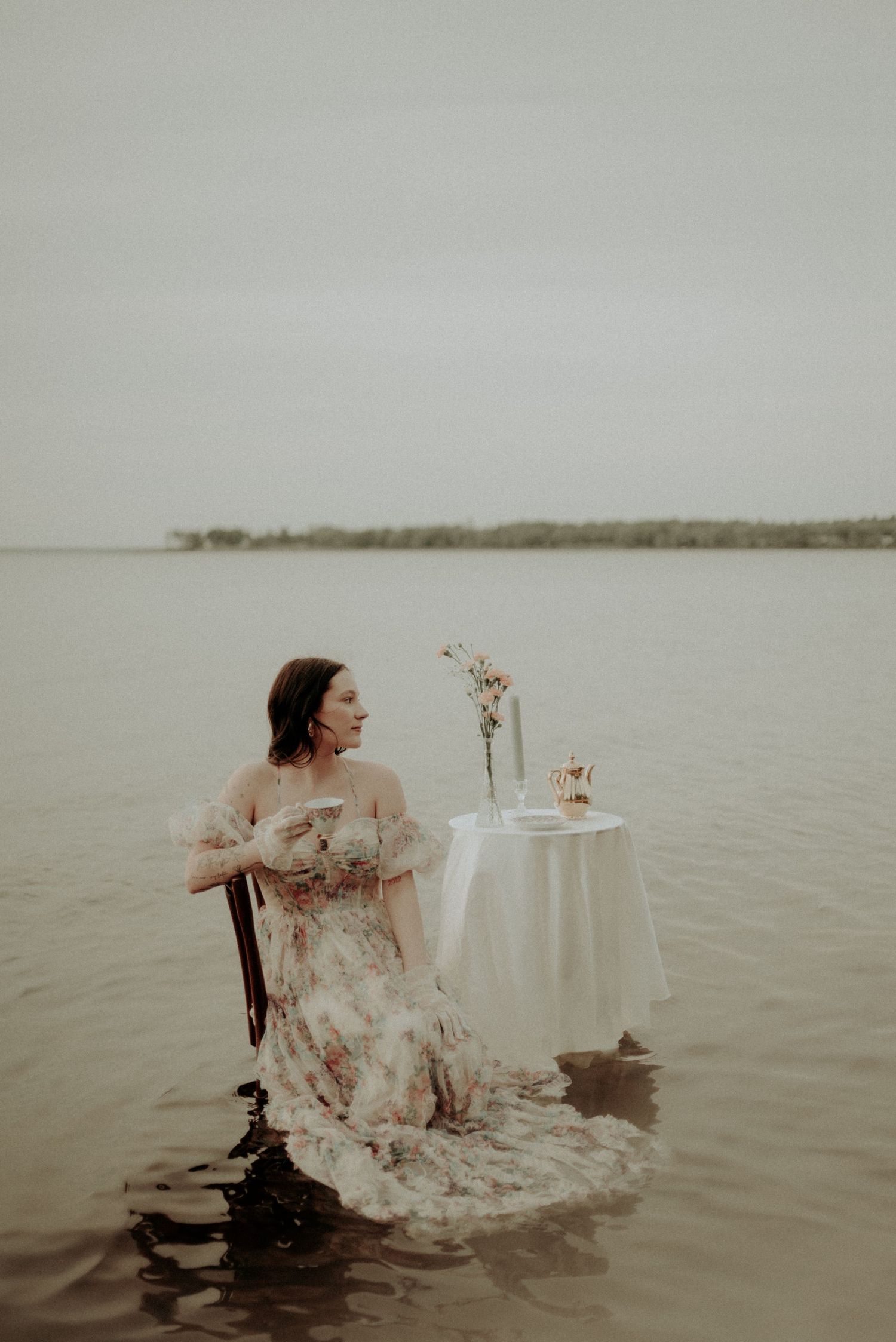A dreamy lakeside scene with a floral dress and white tablecloth setting in moody gray tones.