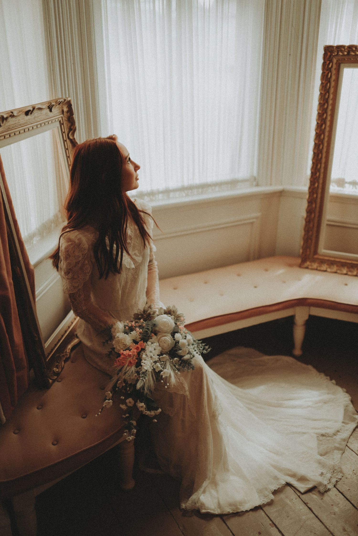 Ethereal bridal photo in vintage room with lace dress, floral bouquet and golden picture frames.