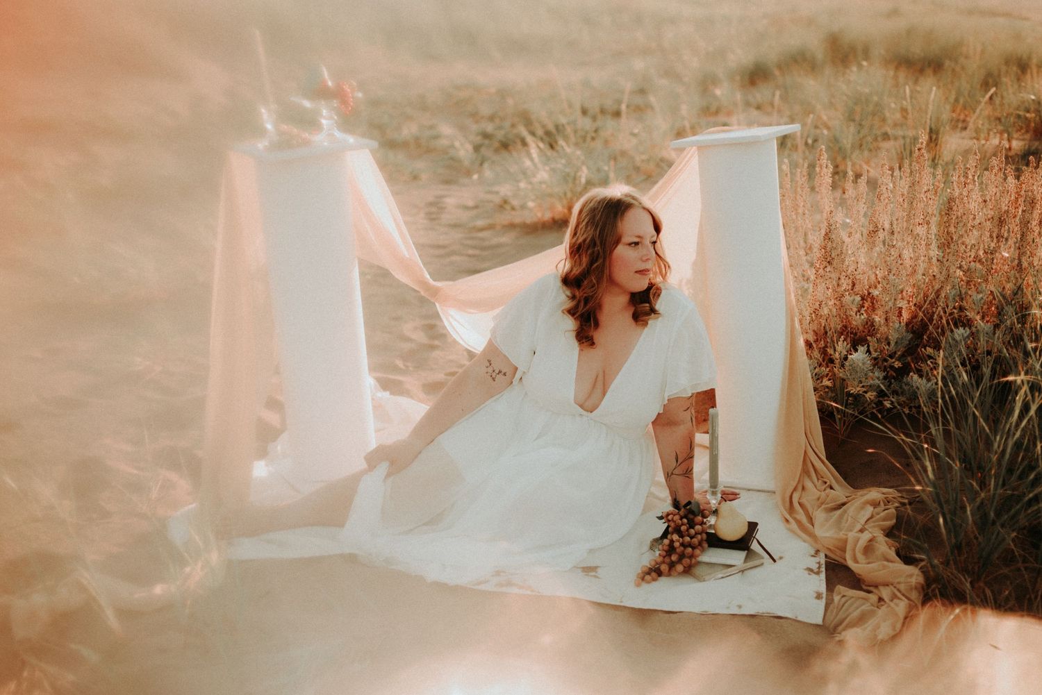 Ethereal beach photoshoot at sunset with flowing white dress and golden light creating a dreamy atmosphere.