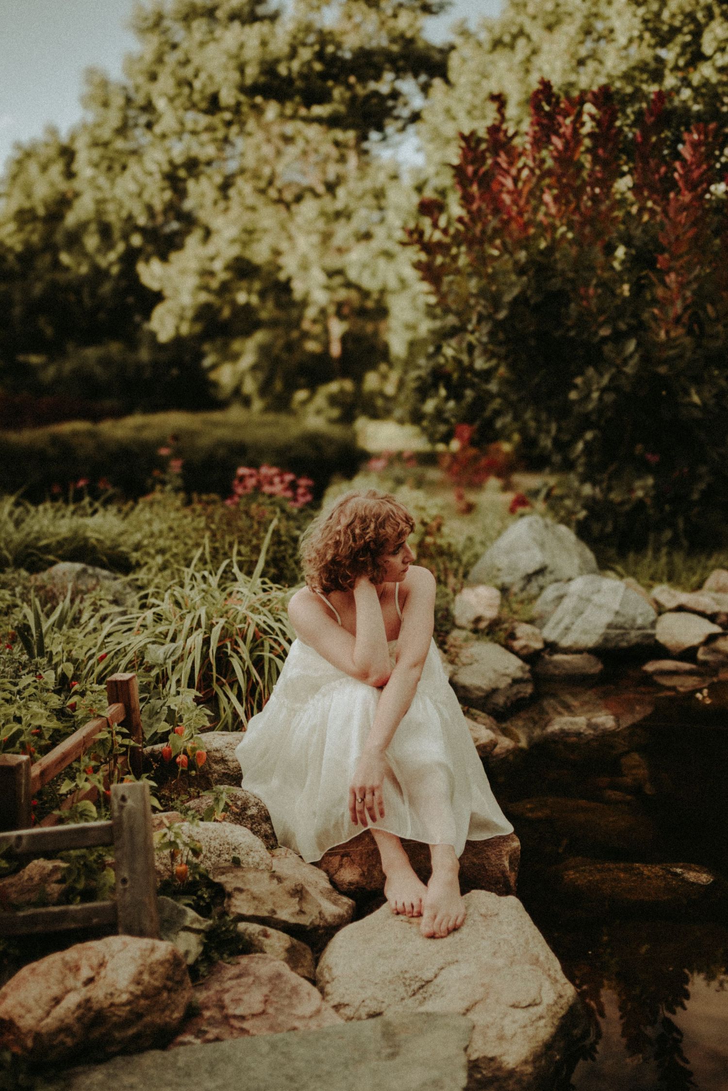 A dreamy garden scene with a white dress against rocks and foliage in warm evening light.