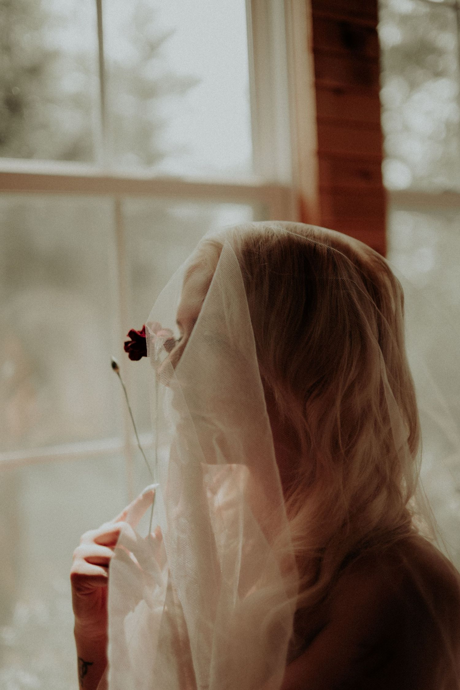 Silhouette behind sheer fabric veil near window in moody lighting.