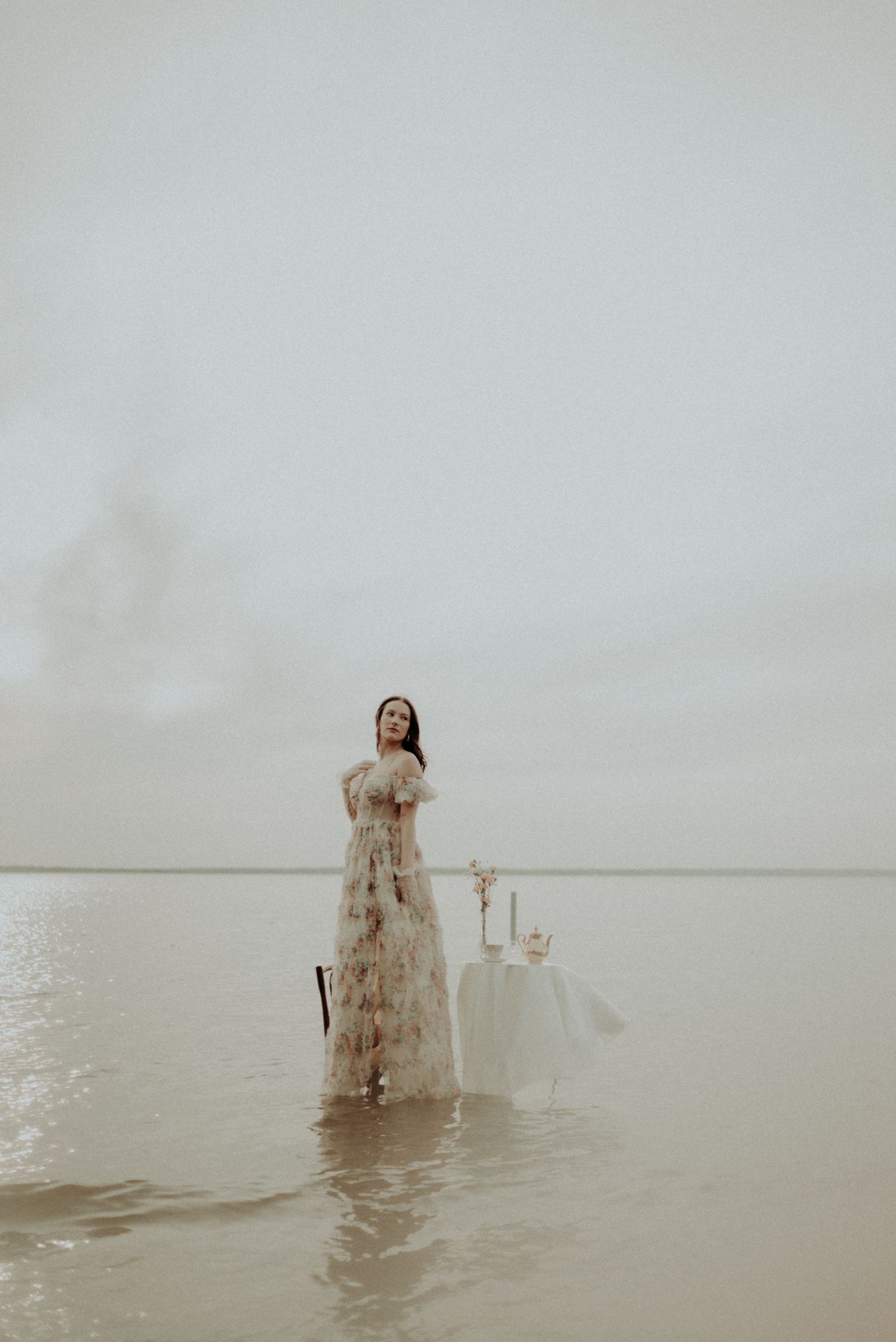 Ethereal fashion photograph featuring delicate dress and table arrangement in serene waters.