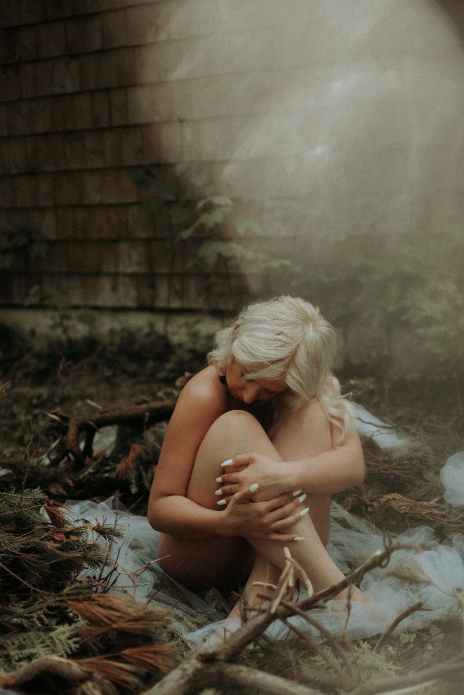 Atmospheric boudoir photography in natural setting with misty lighting effects.