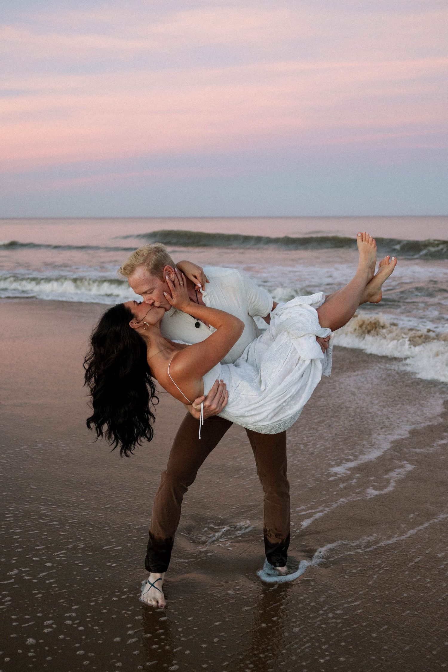 Romantic beach photography with dramatic dip pose at sunset.