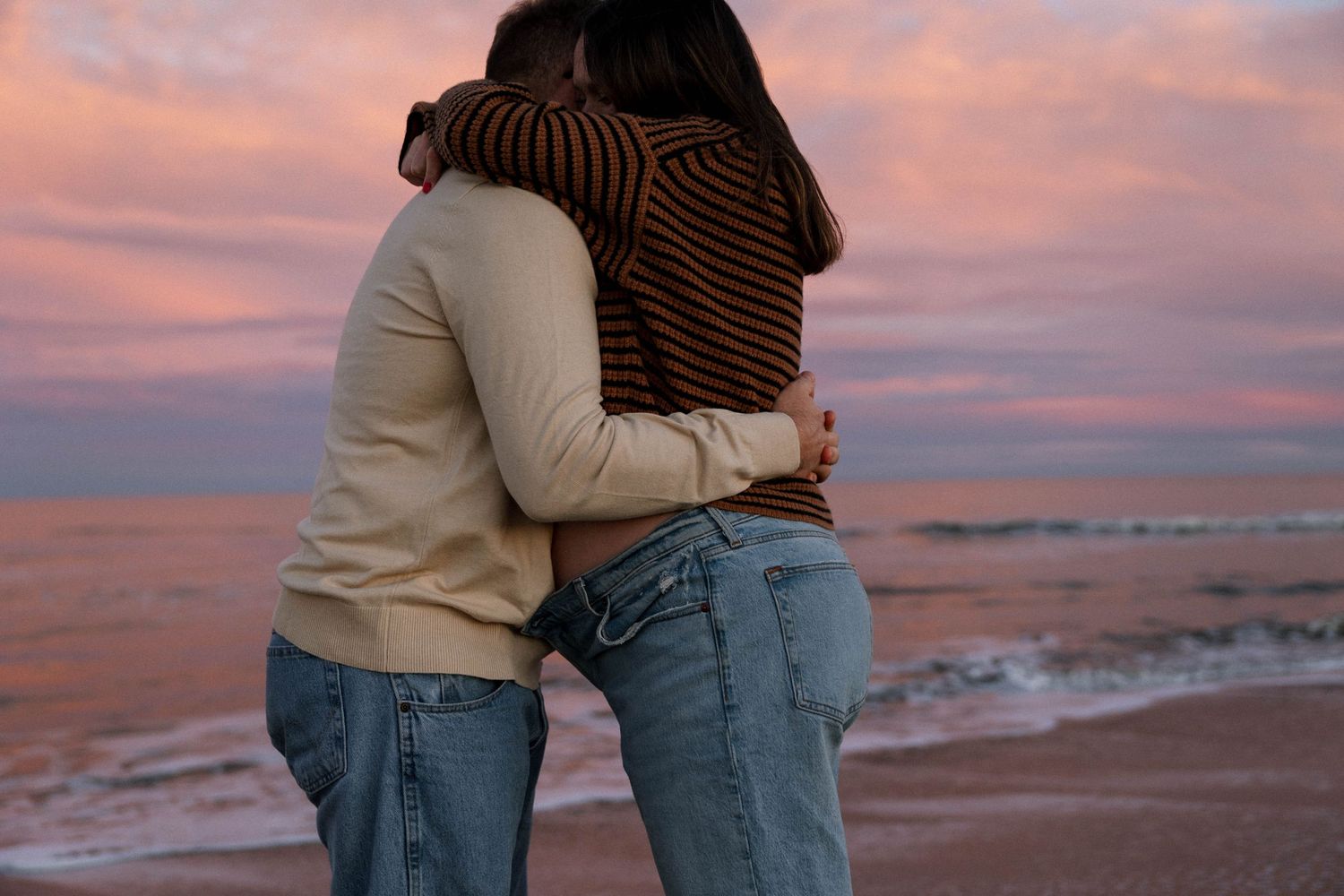 Couple embracing during sunset on beach with pink and orange sky.