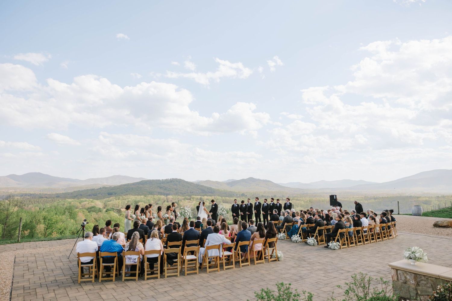 Outdoor wedding ceremony on a stone patio with mountain valley views under a blue sky.