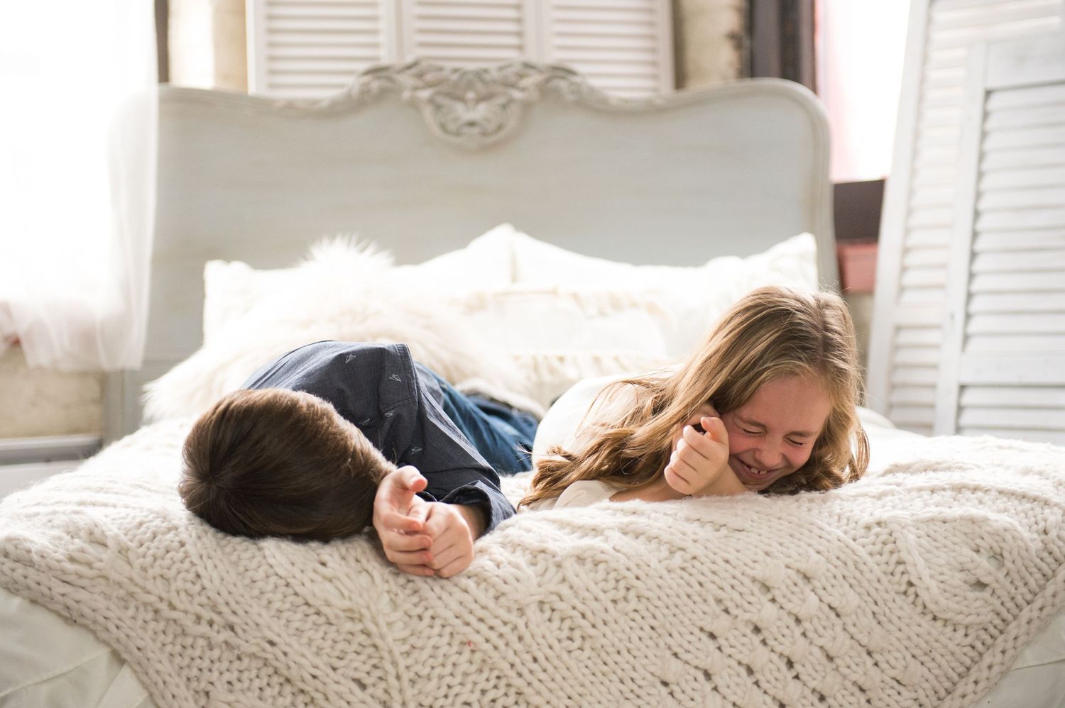 A couple snuggling together on a cozy white bed with soft linens and natural lighting.
