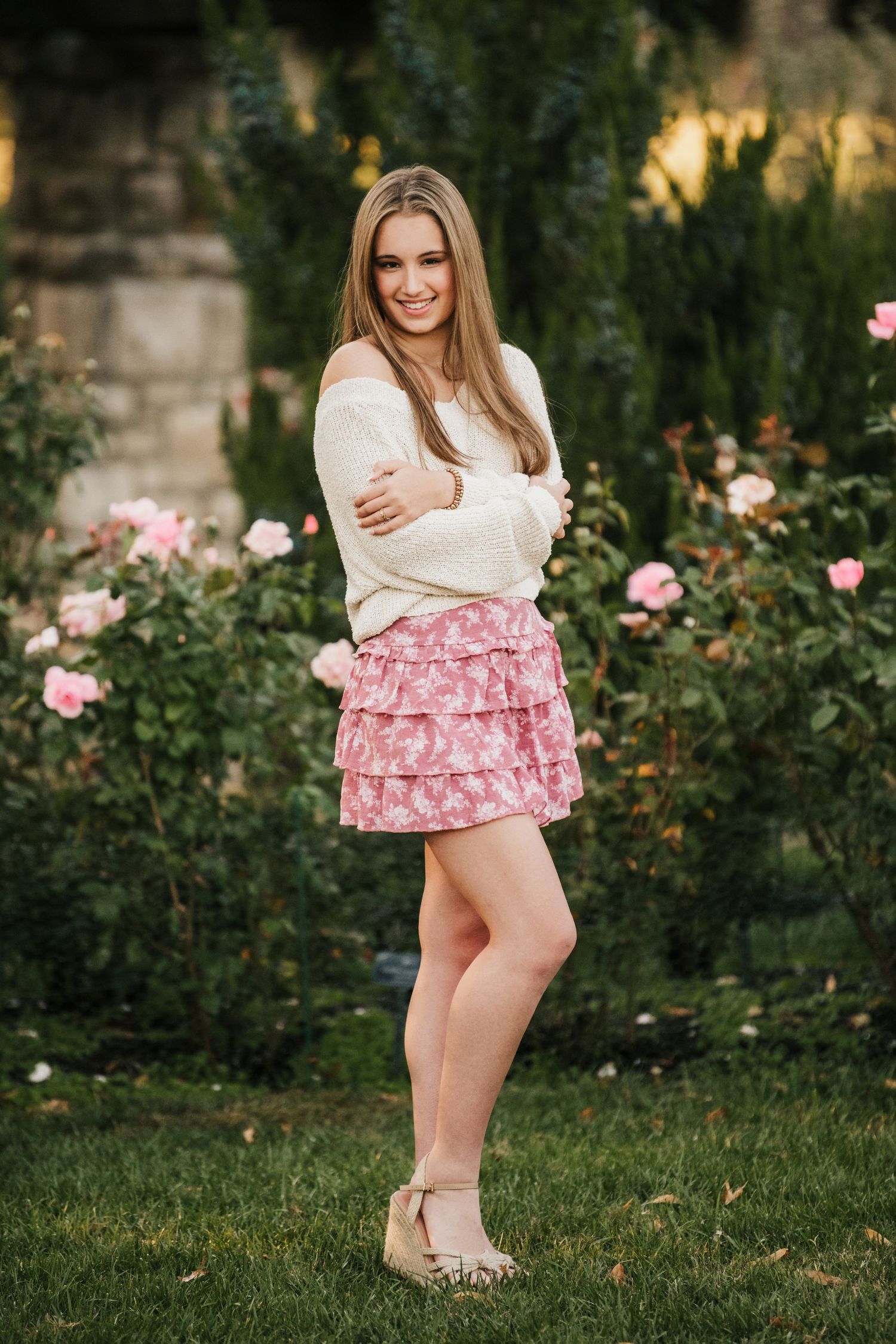 Garden portraits in white sweater and pink ruffled skirt among roses.