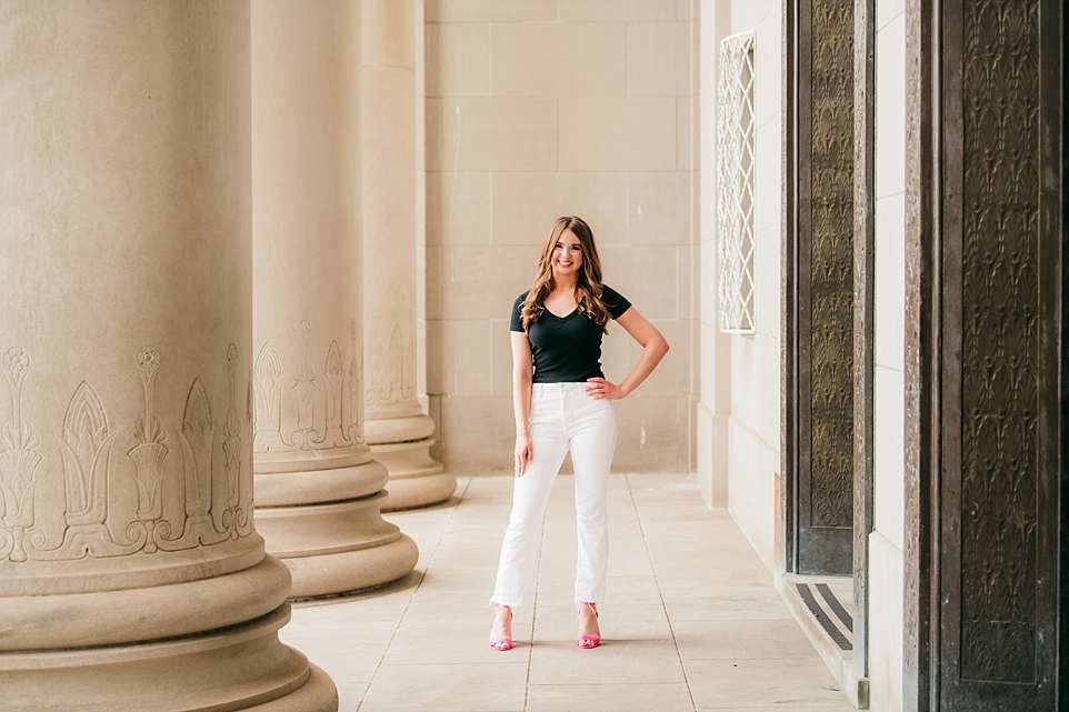 Professional photo of someone in white pants and black top posing between classical columns.