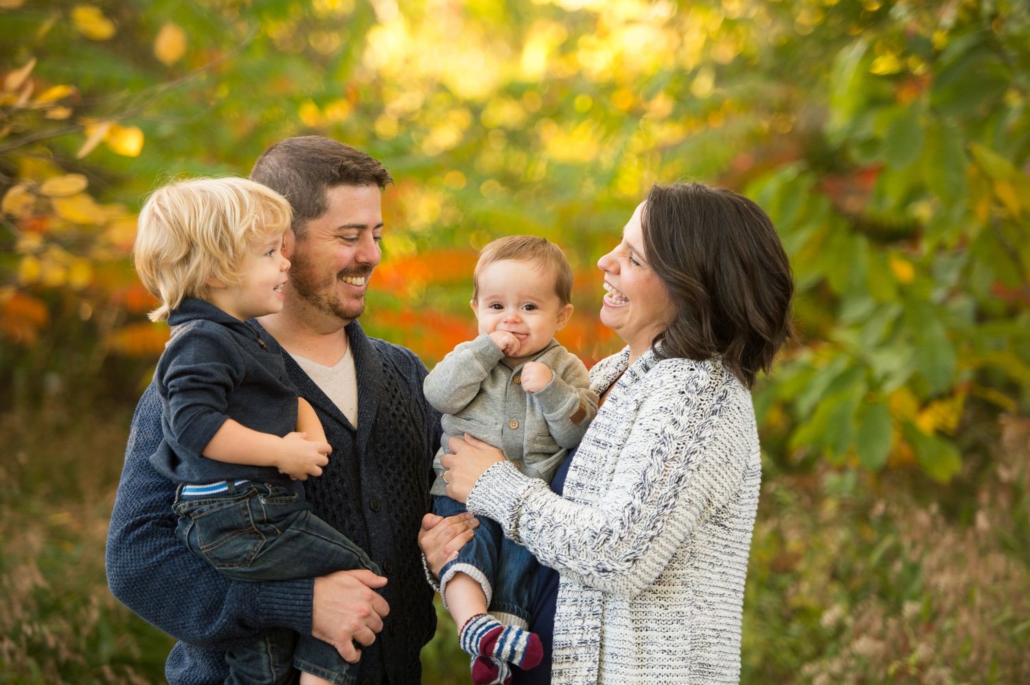 Family enjoying a playful autumn moment together in a park with golden fall foliage in the background.